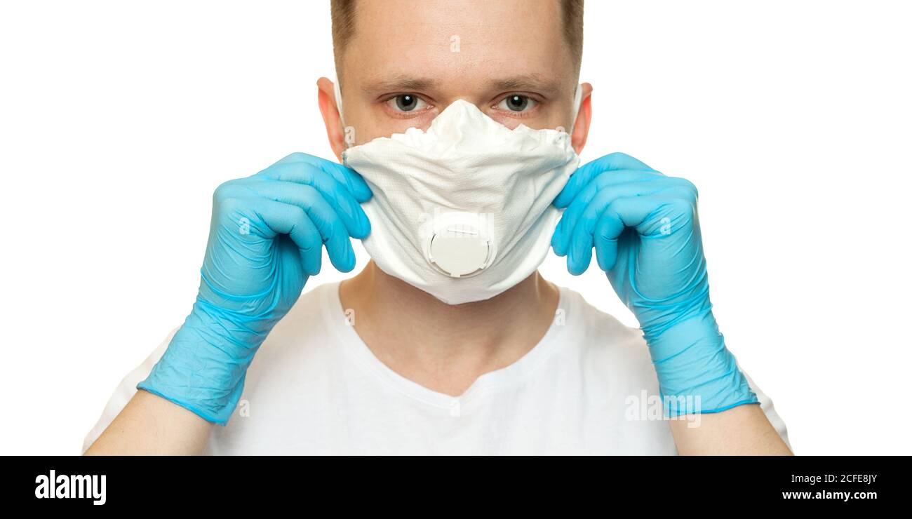 Giovane chirurgo medico in lattice guanti protettivi mette su maschera di protezione bianca su sfondo bianco. Uomo in guanti medici e sulla maschera protettiva per il viso. Foto Stock