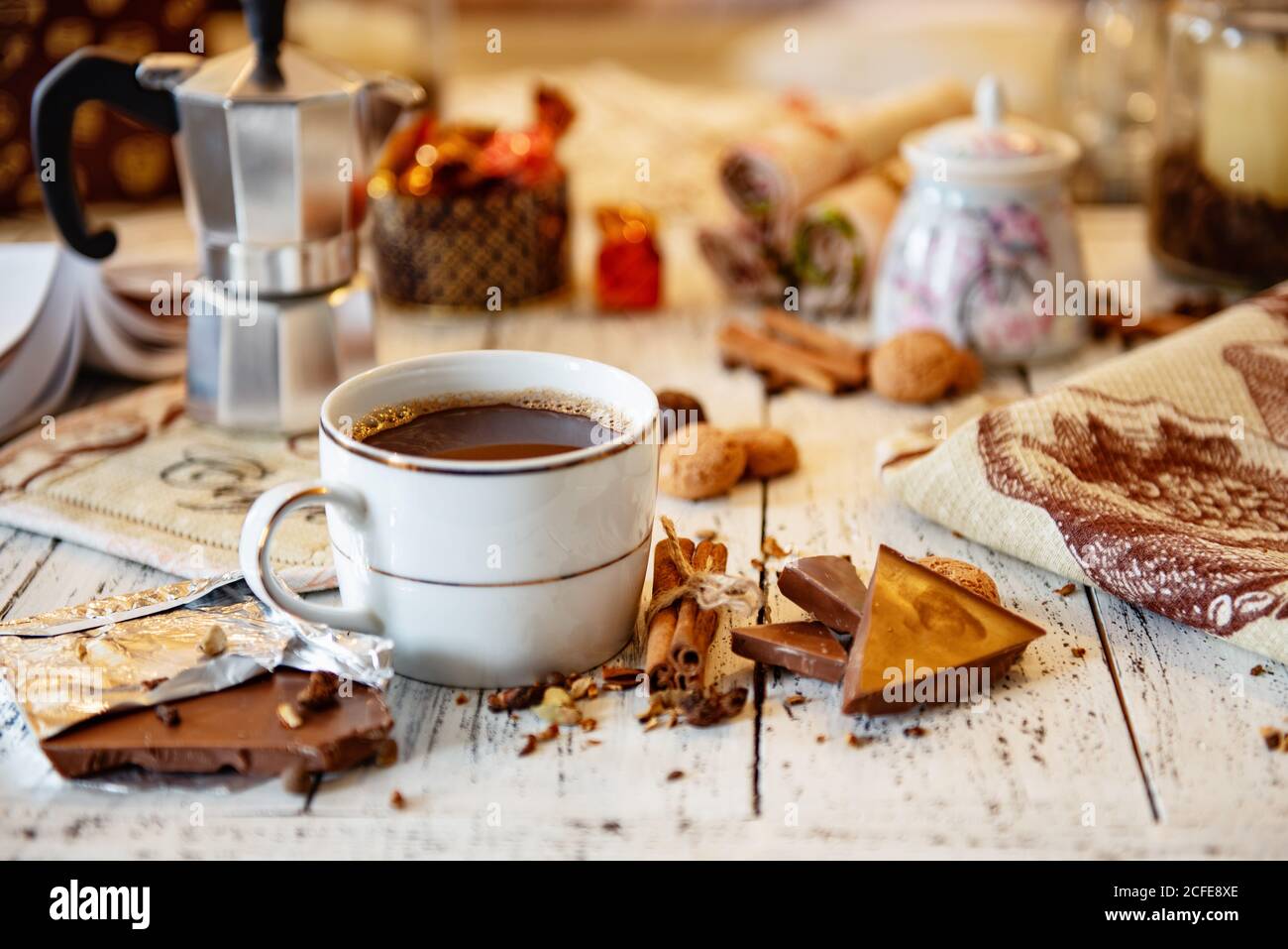 Tazza di caffè, cioccolato, chicchi di caffè, bastoncini di cannella e spezie su un tavolo di legno bianco. Buona colazione del mattino o pausa caffè sullo sfondo. Foto Stock