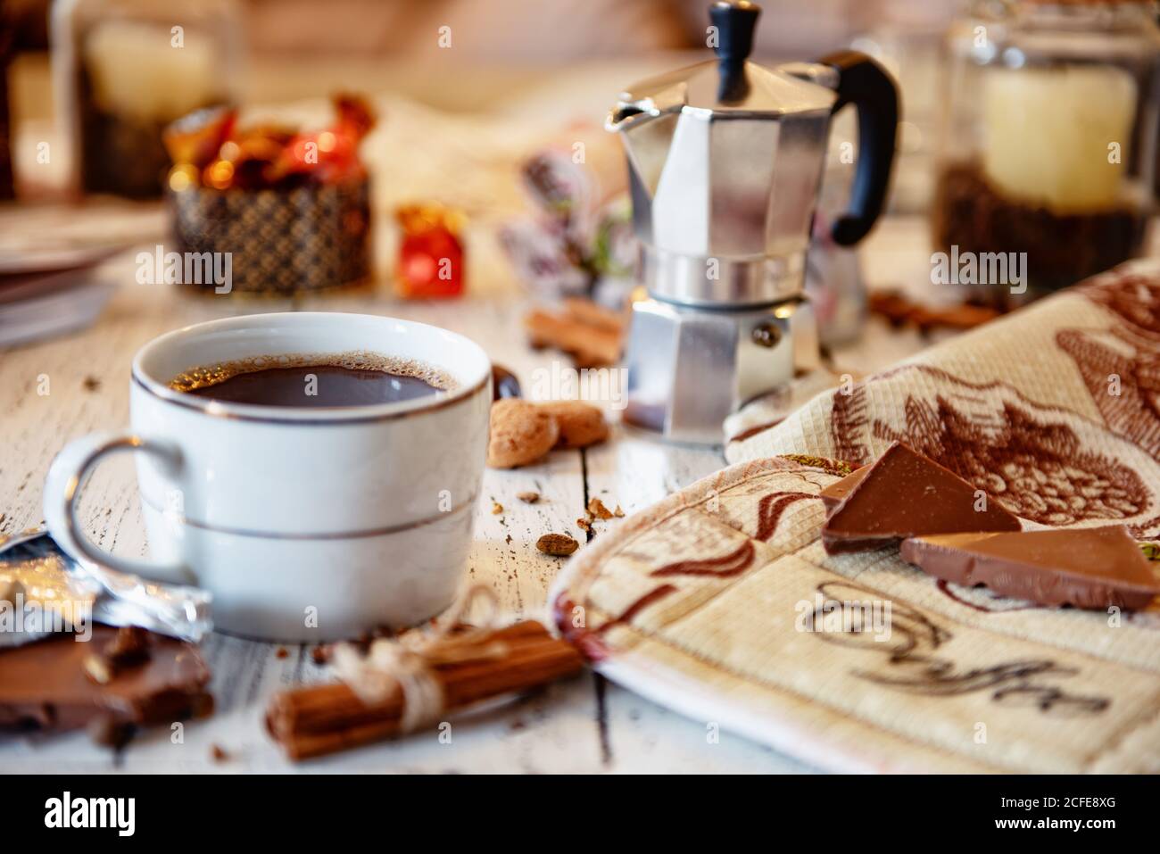 Tazza di caffè, cioccolato, chicchi di caffè, bastoncini di cannella e spezie su un tavolo di legno bianco. Buona colazione del mattino o pausa caffè sullo sfondo. Foto Stock