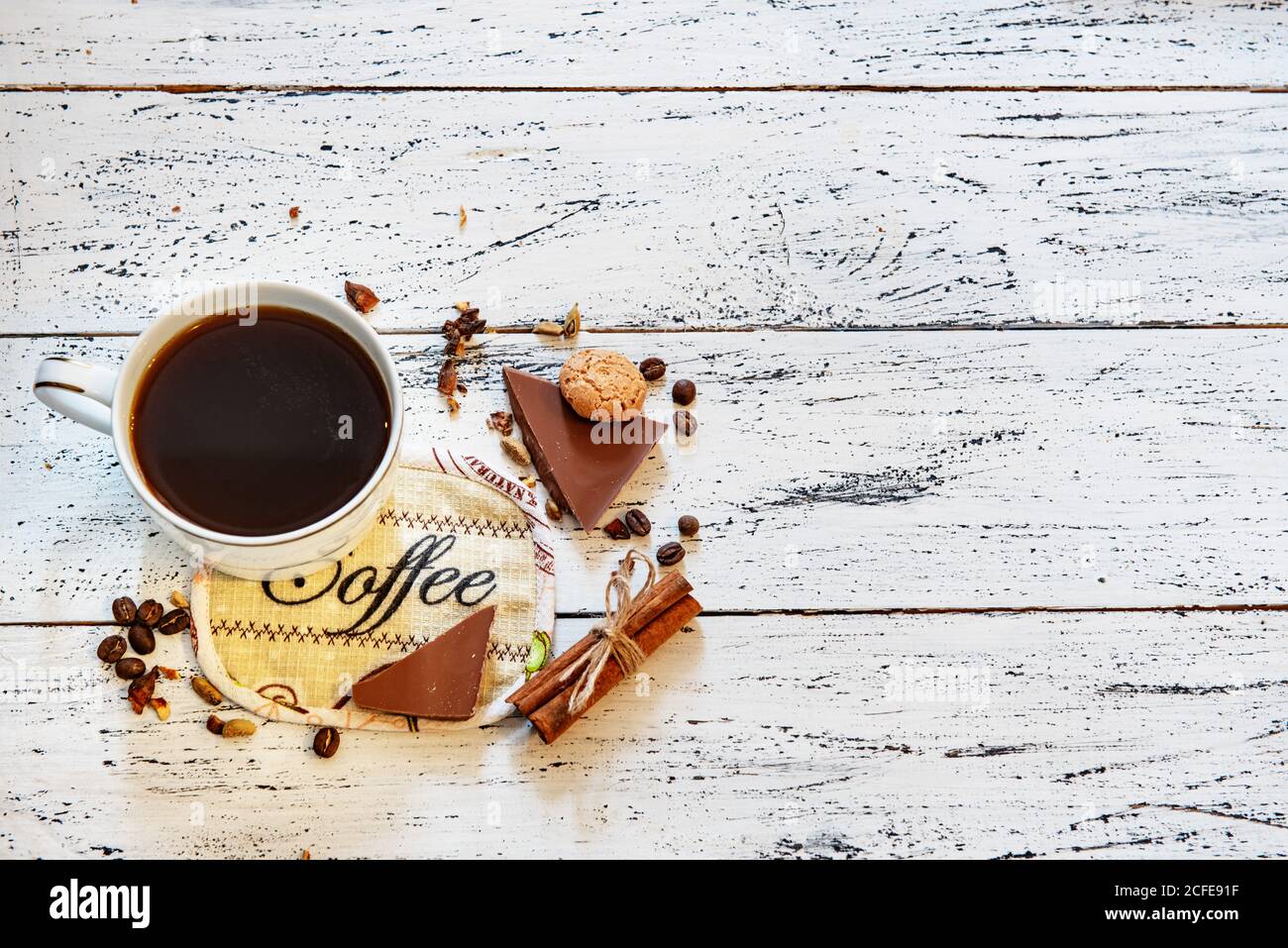 Tazza di caffè, cioccolato, chicchi di caffè e spezie su tavolo di legno bianco. Buona colazione del mattino o pausa caffè sullo sfondo. Foto Stock