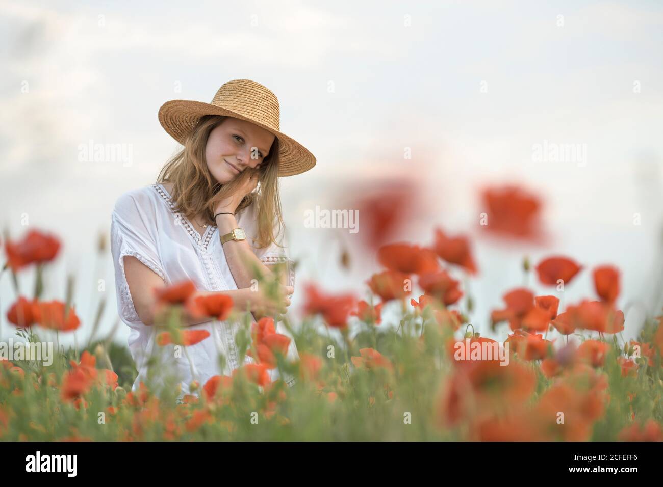 Giovane donna nel cappello di paglia in campo di papavero sorride a. fotocamera Foto Stock