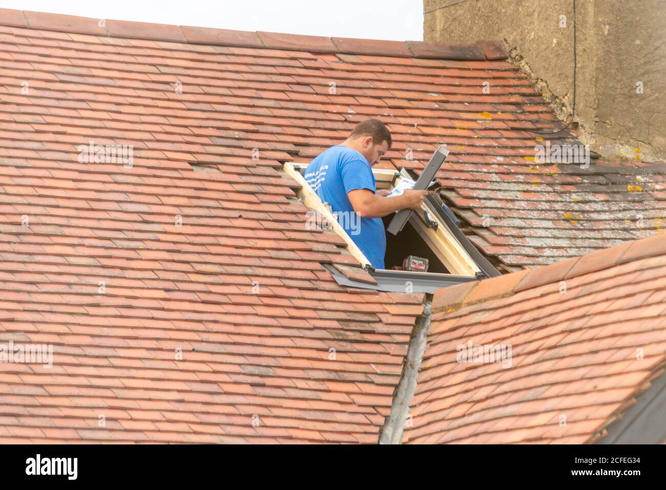 Un costruttore che monta una finestra lucernario nel tetto di una proprietà a Westcliff on Sea, Essex, Regno Unito, durante la lettura delle istruzioni. Uomo d'artigianato bianco Foto Stock