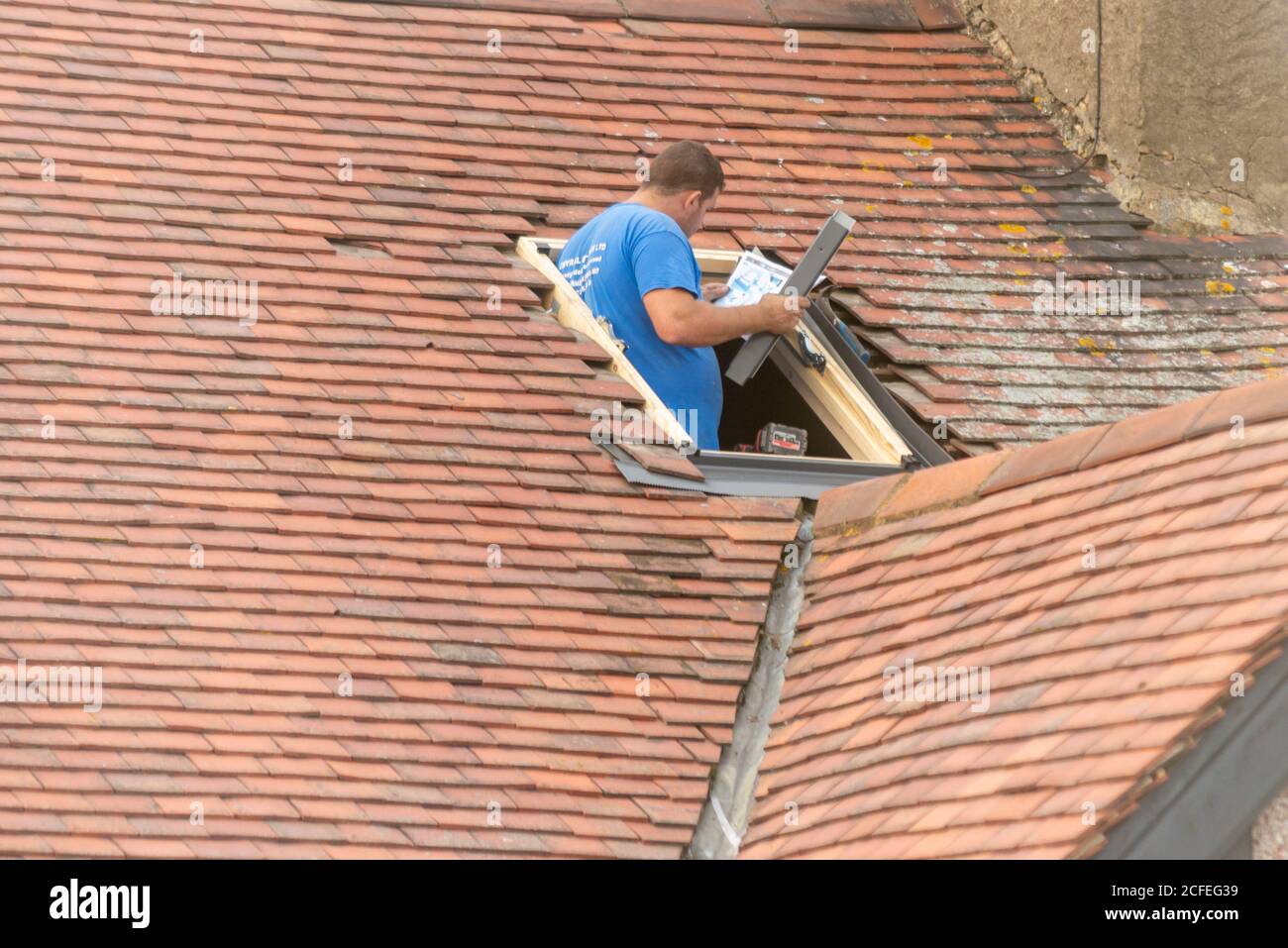 Un costruttore che monta una finestra lucernario nel tetto di una proprietà a Westcliff on Sea, Essex, Regno Unito, durante la lettura delle istruzioni. Uomo d'artigianato bianco Foto Stock