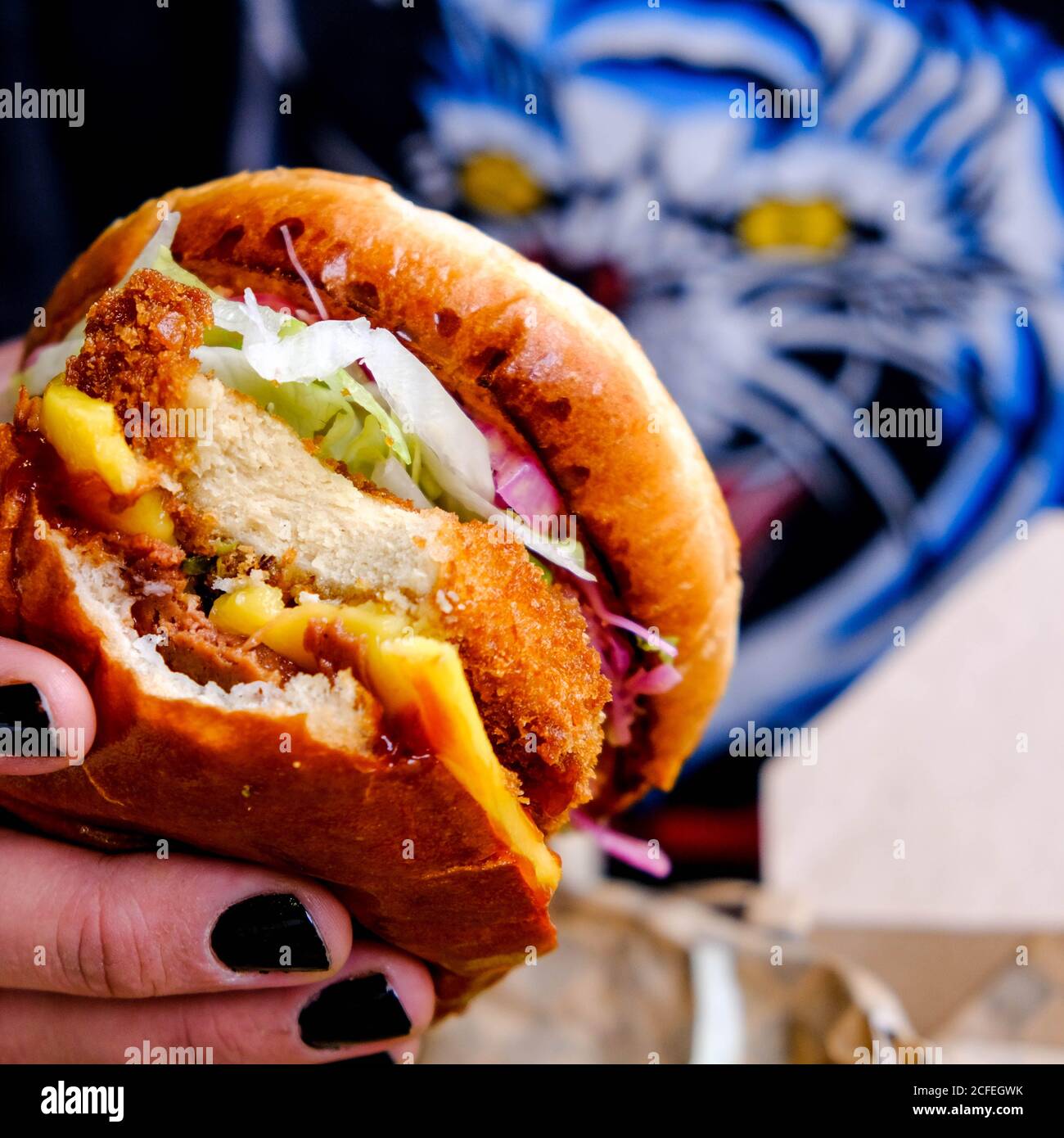 Persona con unghie verniciate nere che tiene UN Vegano fresco Burger a base di piante in un bun Foto Stock