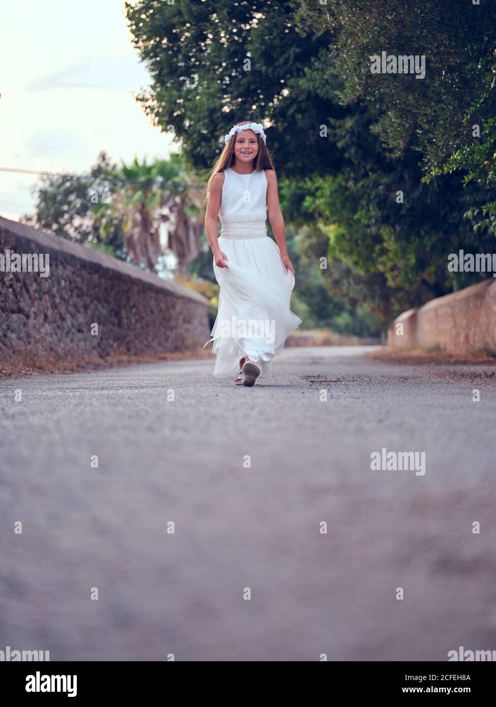 Carina bambina in bianco abito arioso e fascia floreale passeggiate nel parco Foto Stock