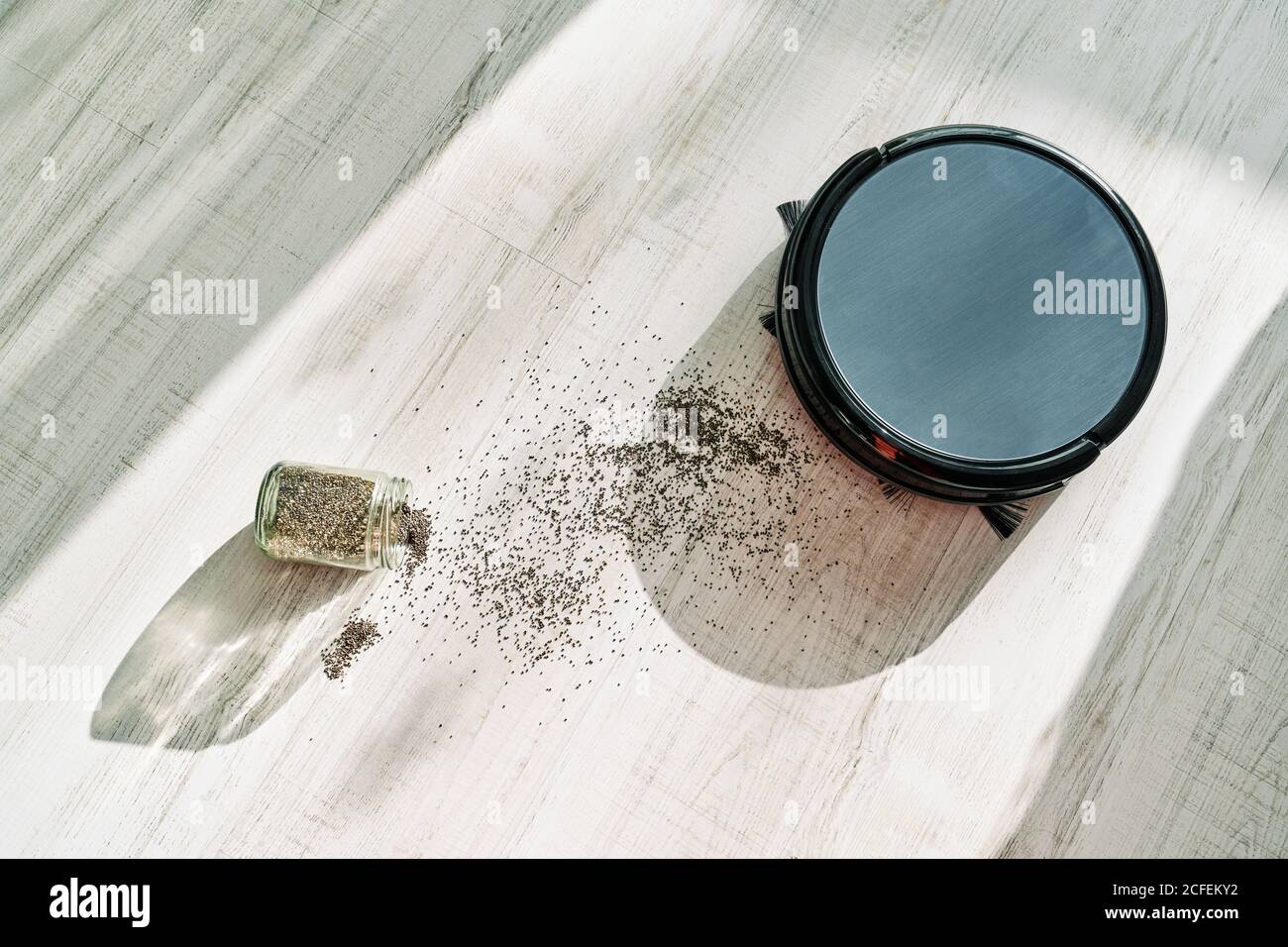 Dall'alto dell'aspirapolvere robot rotondo che scorre sulla luce laminare il pavimento e rimuovere lo sporco fuoriuscito dal recipiente di vetro Foto Stock