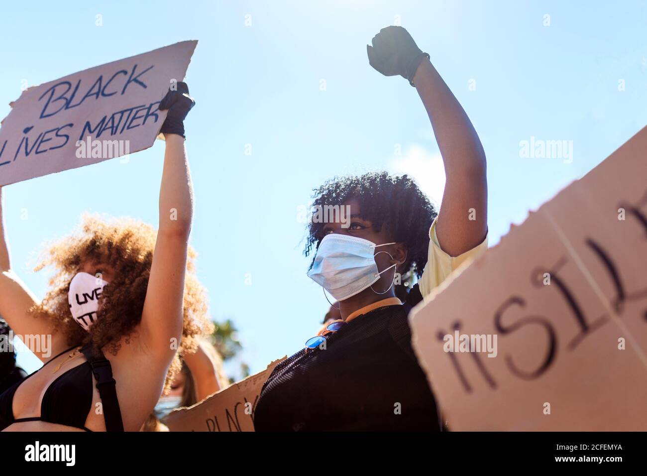 Donne etniche serie con acconciatura afro che tiene poster di cartone con black lives materia iscrizione e alzando pugno durante la dimostrazione in città affollata e aggrapparsi Foto Stock