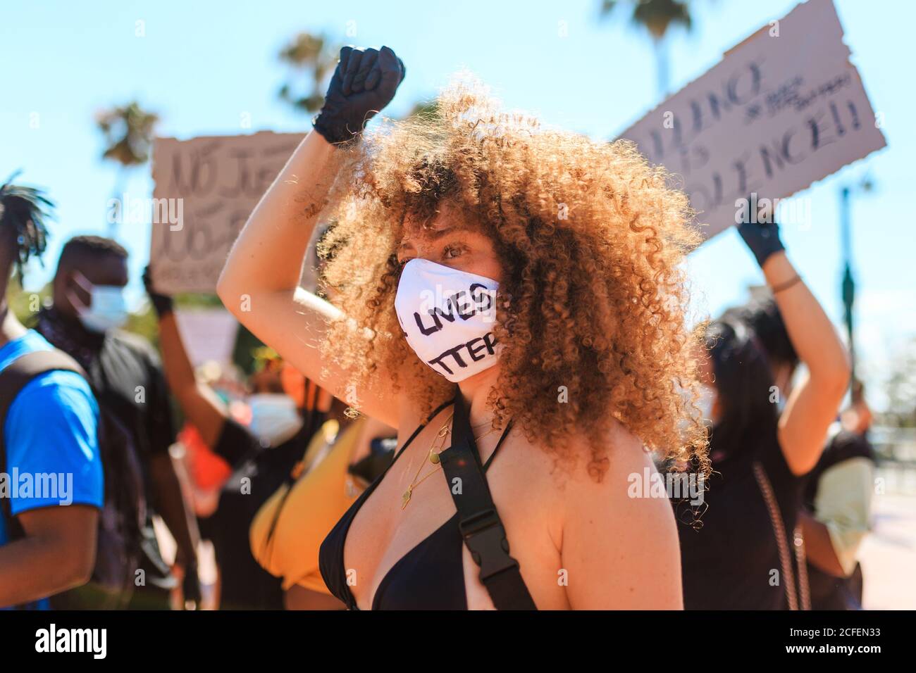 Femmina etnico con acconciatura afro e in maschera protettiva con black lives materia iscrizione in piedi su strada alzando pugno durante una dimostrazione Foto Stock