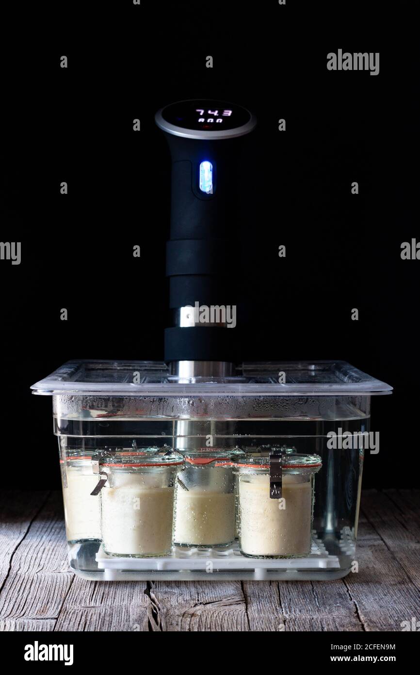 Cheesecake in vasche di vetro preparazione in capo cottura sous-vide messo su tavolo di legno su sfondo nero Foto Stock