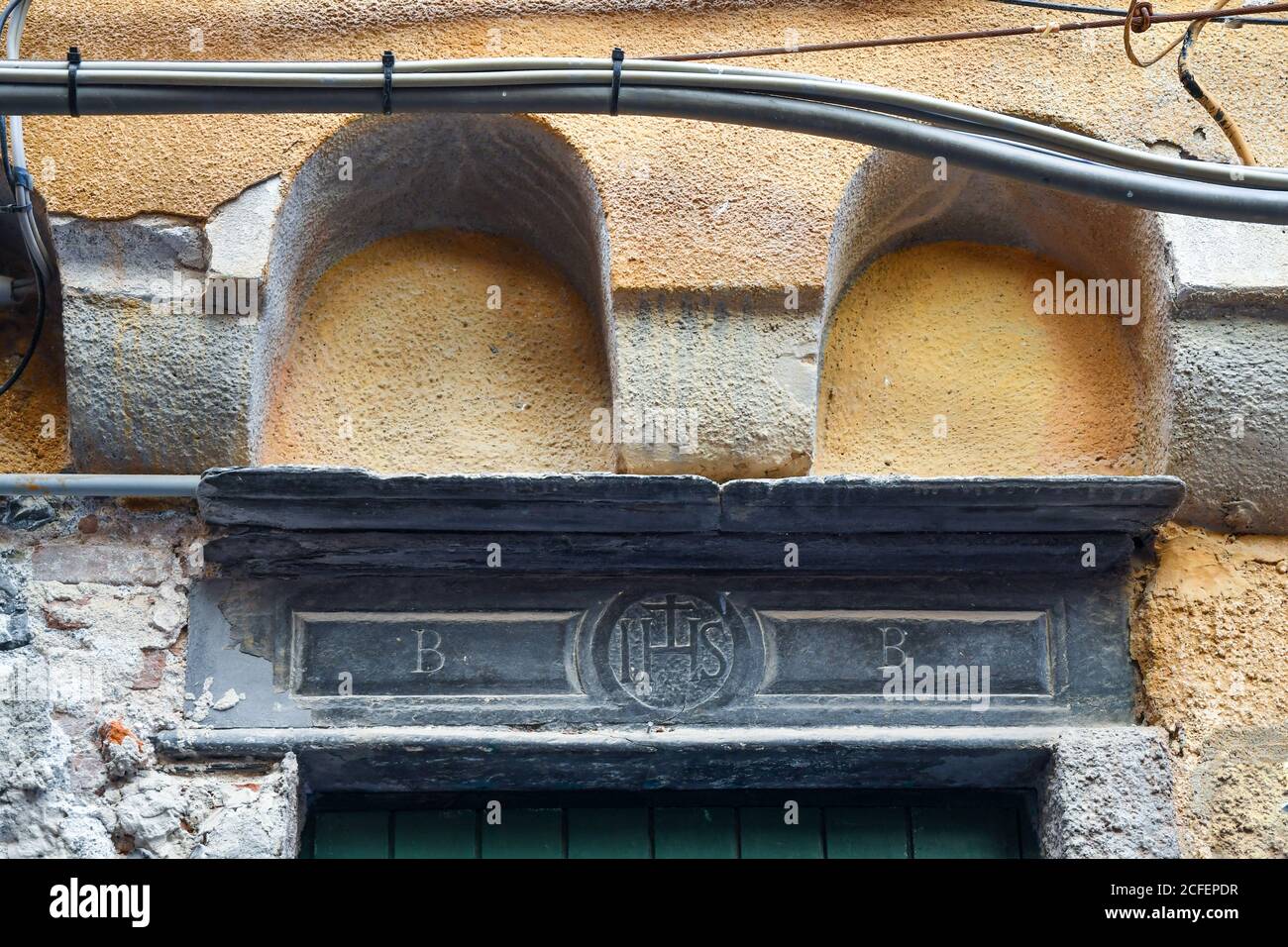 Primo piano di una pietra scolpita sopra la porta d'ingresso di un edificio medievale con il simbolo religioso IHS, greco acronimo di Gesù, Porto Venere, Italia Foto Stock