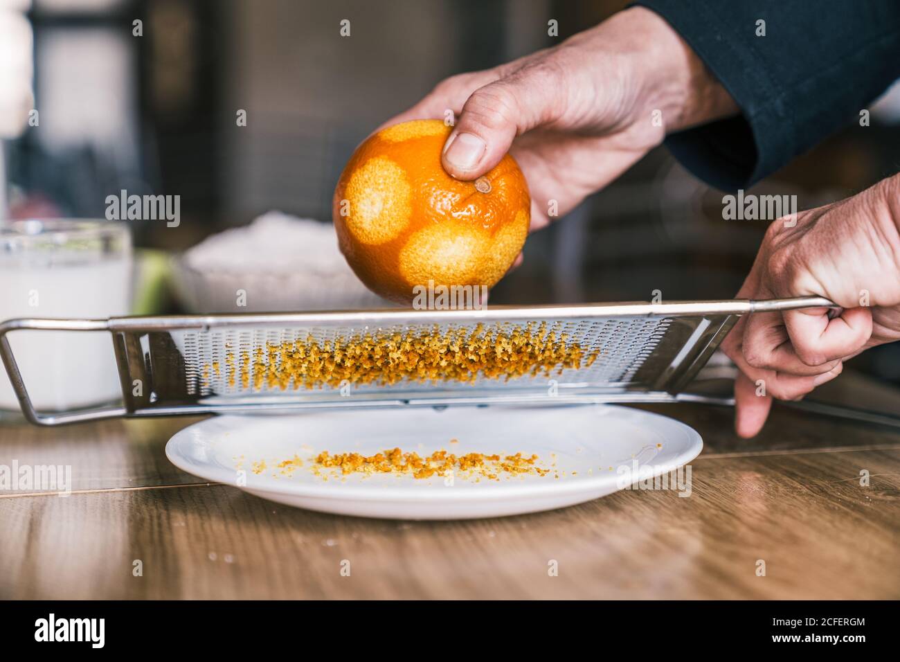 Vista laterale del raccolto anonimo Donna rimuovere scorza d'arancia con grattugia mentre preparare pasta aromatica in cucina casa Foto Stock