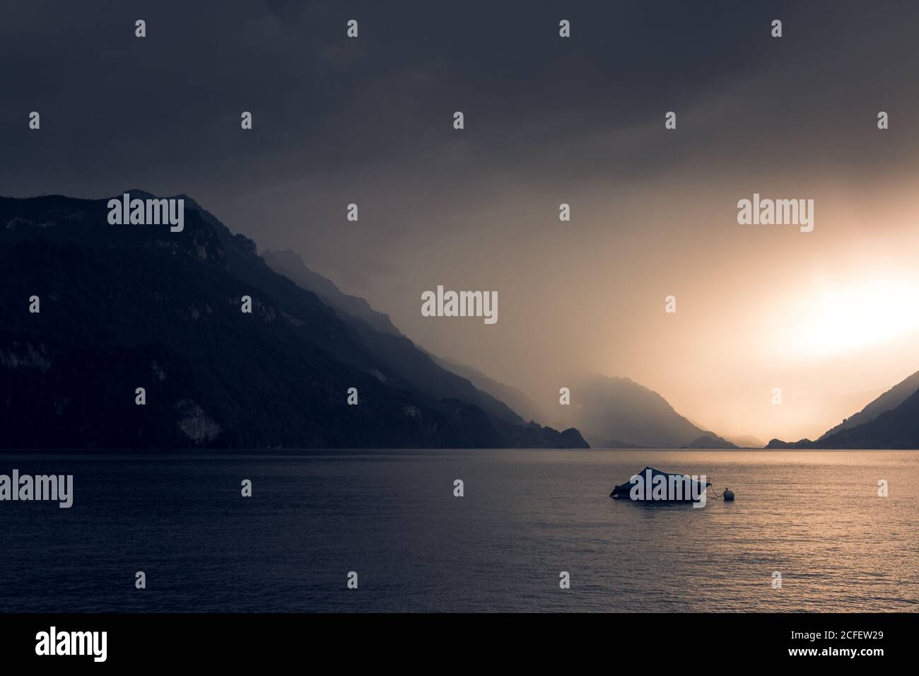 Calmo paesaggio di barca scura in acqua ondulata sotto il grigio Cielo nuvoloso in montagna in Svizzera Foto Stock