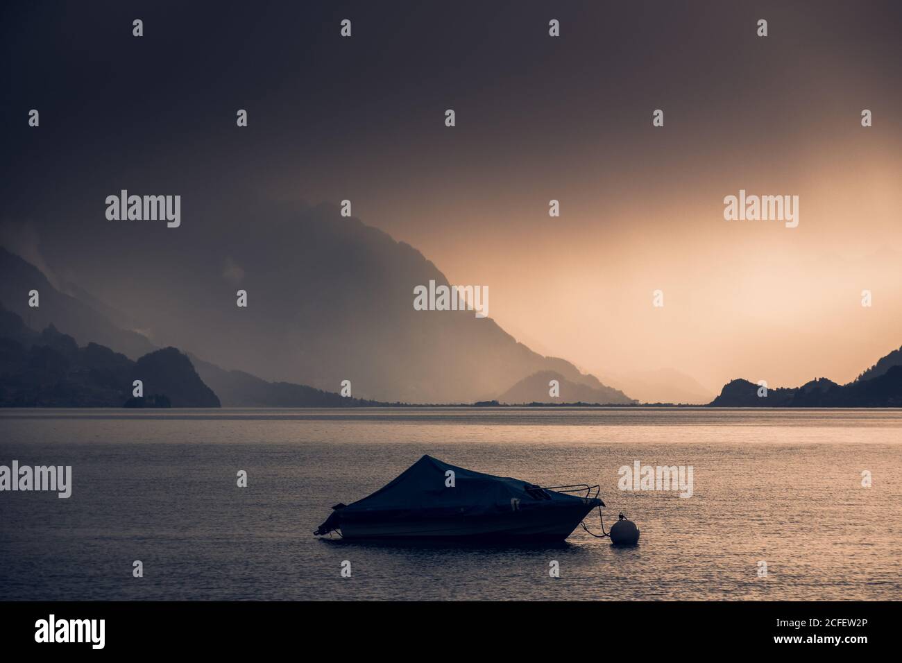 Calmo paesaggio di barca scura in acqua ondulata sotto il grigio Cielo nuvoloso in montagna in Svizzera Foto Stock