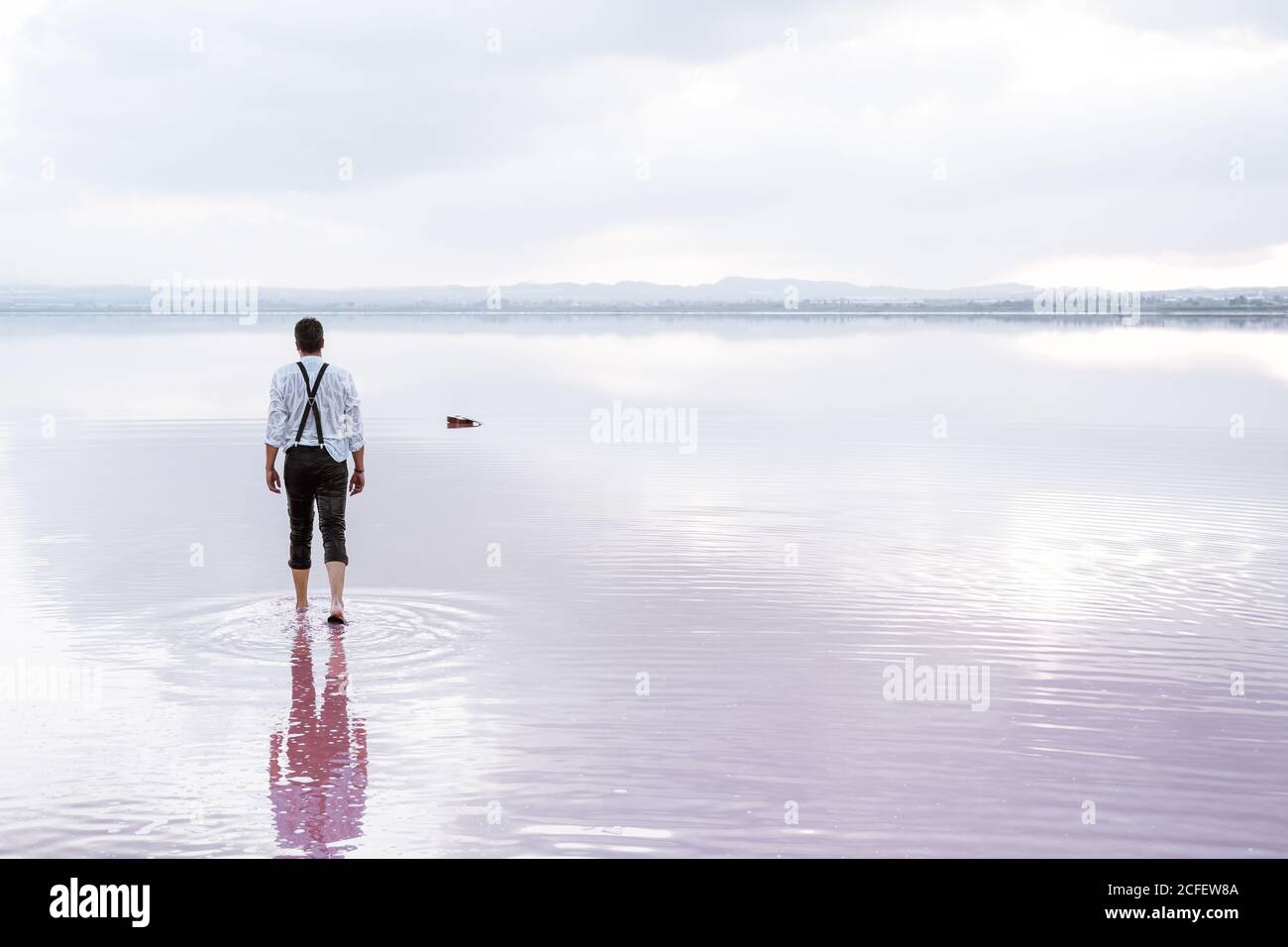 Vista posteriore uomo serio in camicia bianca e arrotolato pantaloni che si avvicinano a una chitarra in mare sfumato Foto Stock