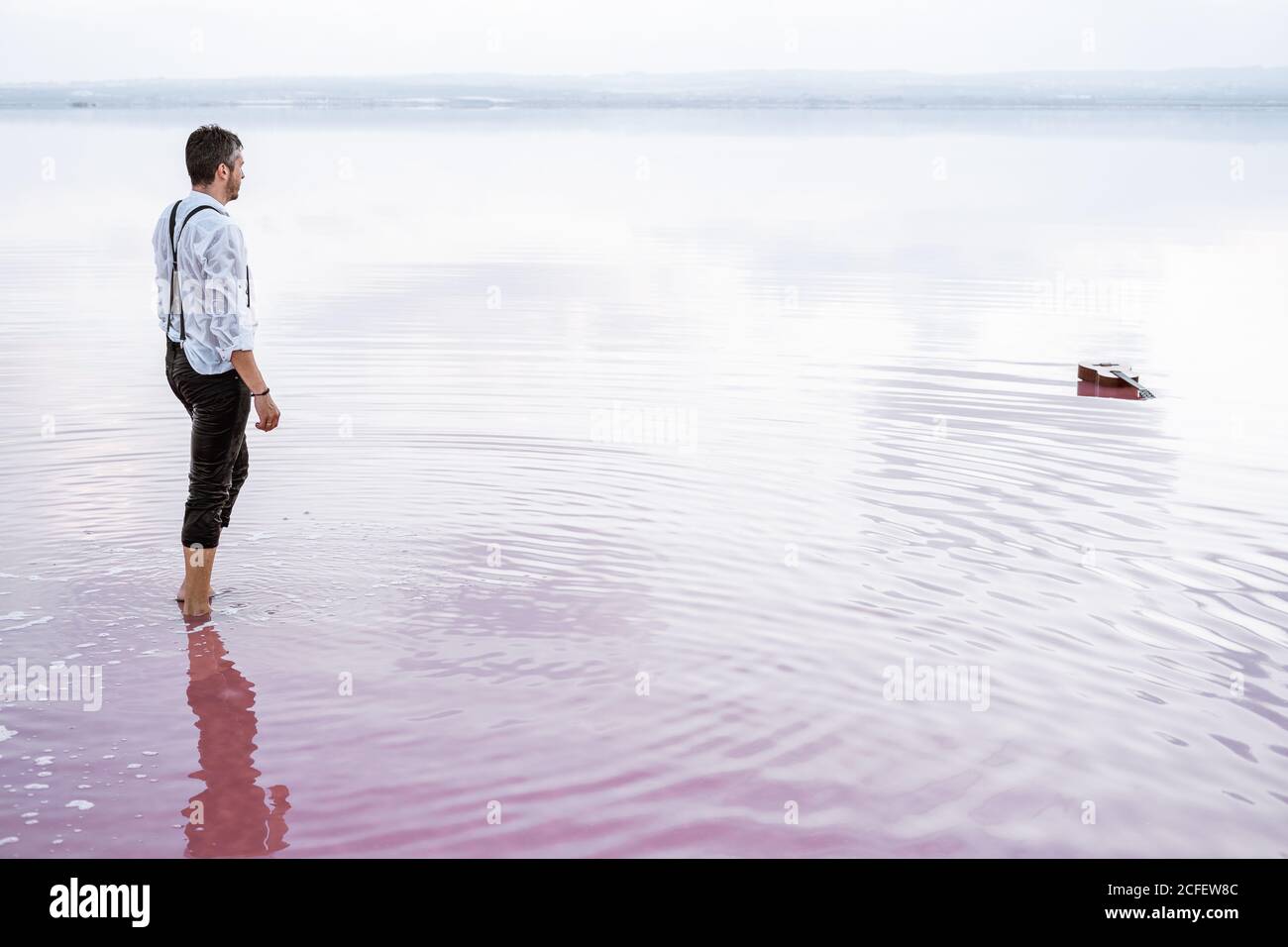 Vista laterale uomo serio in camicia bianca e arrotolato pantaloni che si avvicinano a una chitarra in mare sfumato Foto Stock