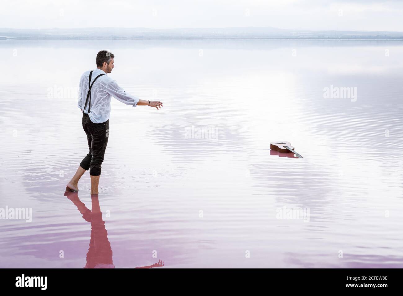 Vista laterale uomo serio in camicia bianca e arrotolato pantaloni che vengono con mano estensibile alla chitarra in gradiente mare Foto Stock