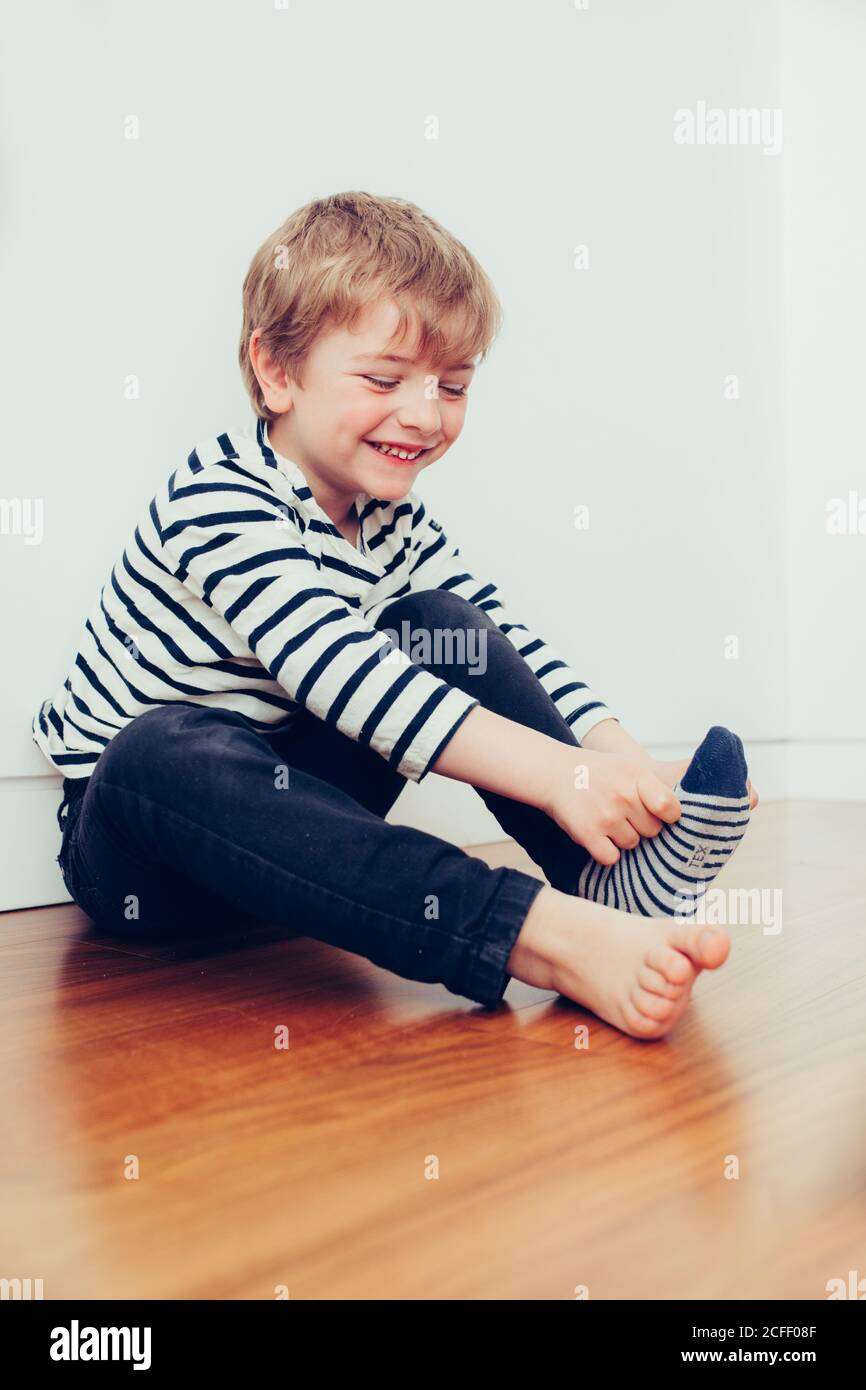 Divertente ragazzo che indossa calze e seduto sul pavimento in camera Foto Stock