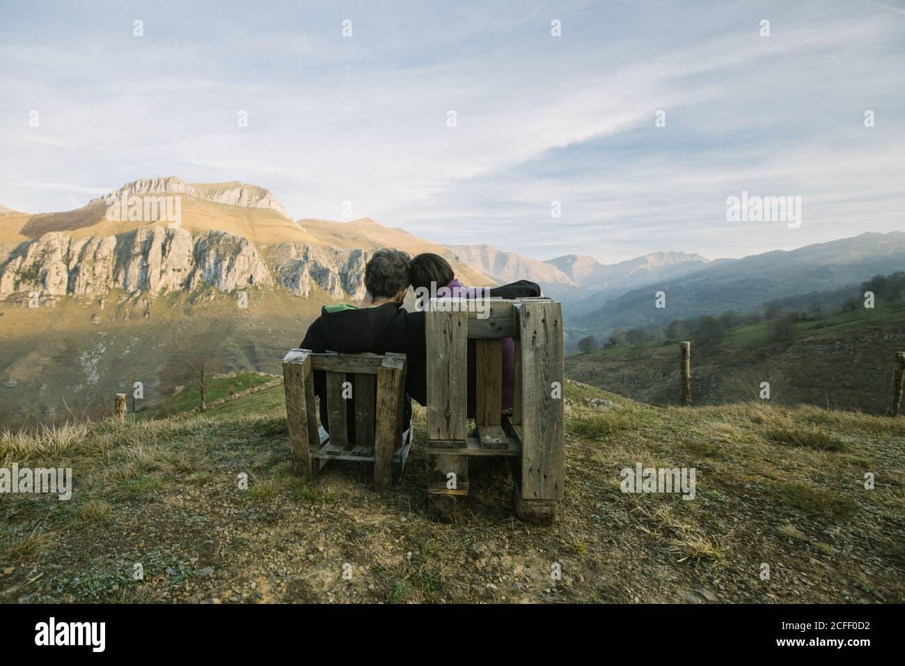 Coppia seduta su panchine di legno sulla remota collina verde e. Goditi la vista mentre visiti la Spagna Foto Stock