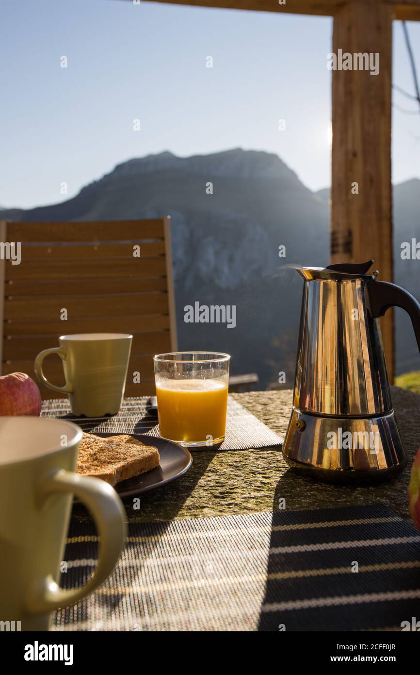 Tazze bianche e macchina per il caffè calda posizionate sul tavolo con  toast caldi e bicchiere di succo d'arancia fresco all'aperto veranda con  montagna sullo sfondo Foto stock - Alamy