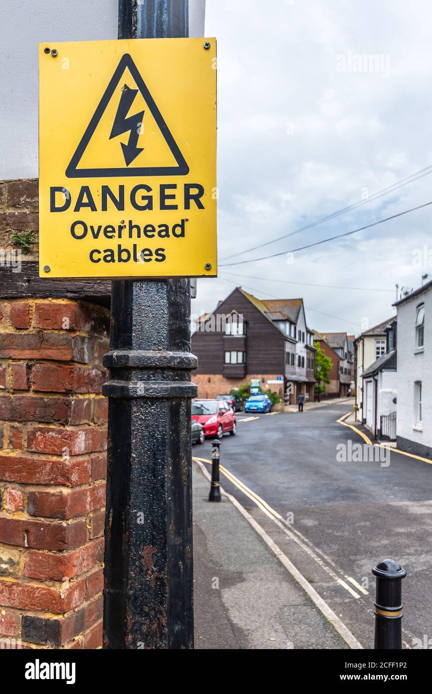 Avvertimento giallo pericolo cavi sospesi avvertimento fissato ad un palo in una strada con cablaggio elettrico sopra, in Inghilterra, Regno Unito. Foto Stock