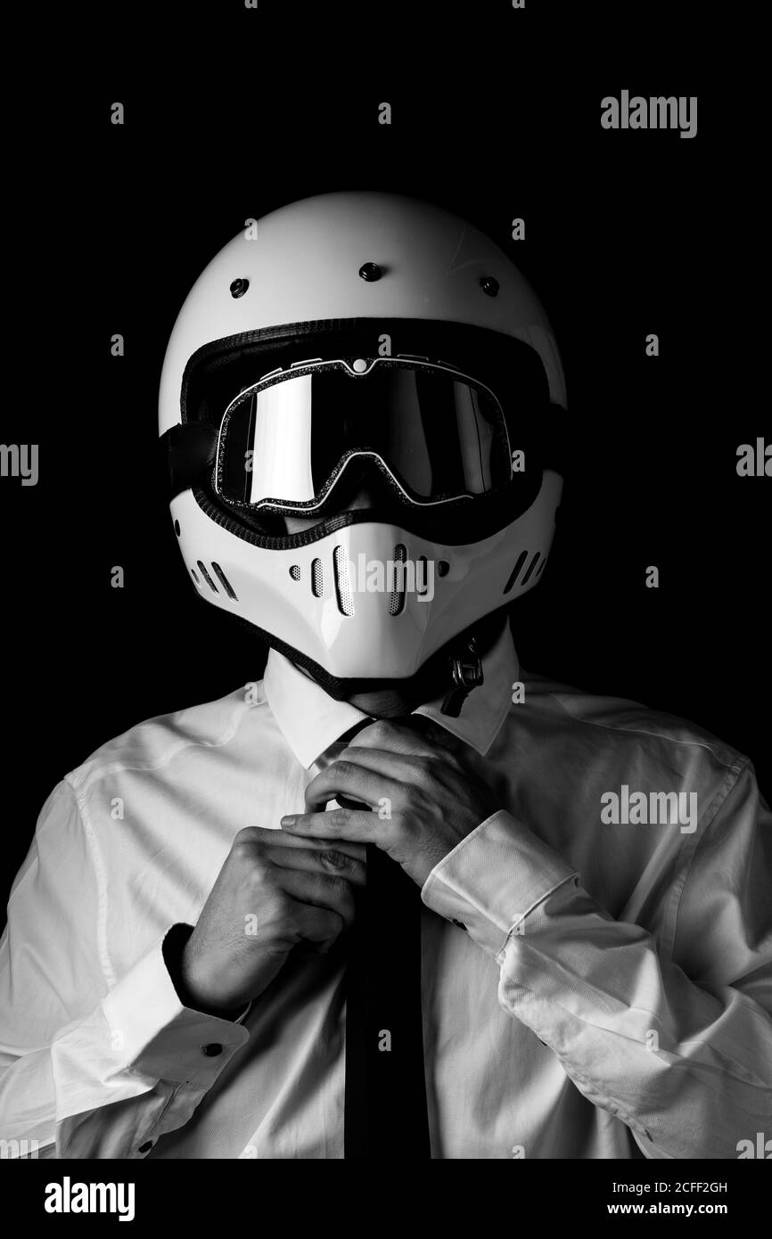 Bianco e nero di anonimo racer in bianco formale e. cravatta indossando un casco moderno e lucido con occhiali neri in studio Foto Stock