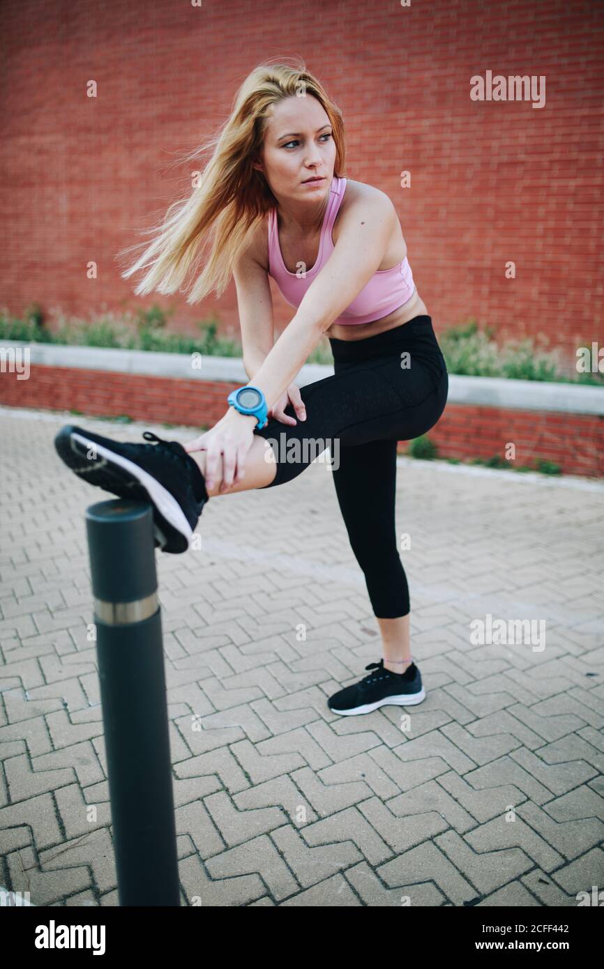 Giovane donna bionda stretching dopo una sessione di corsa in strada Foto Stock