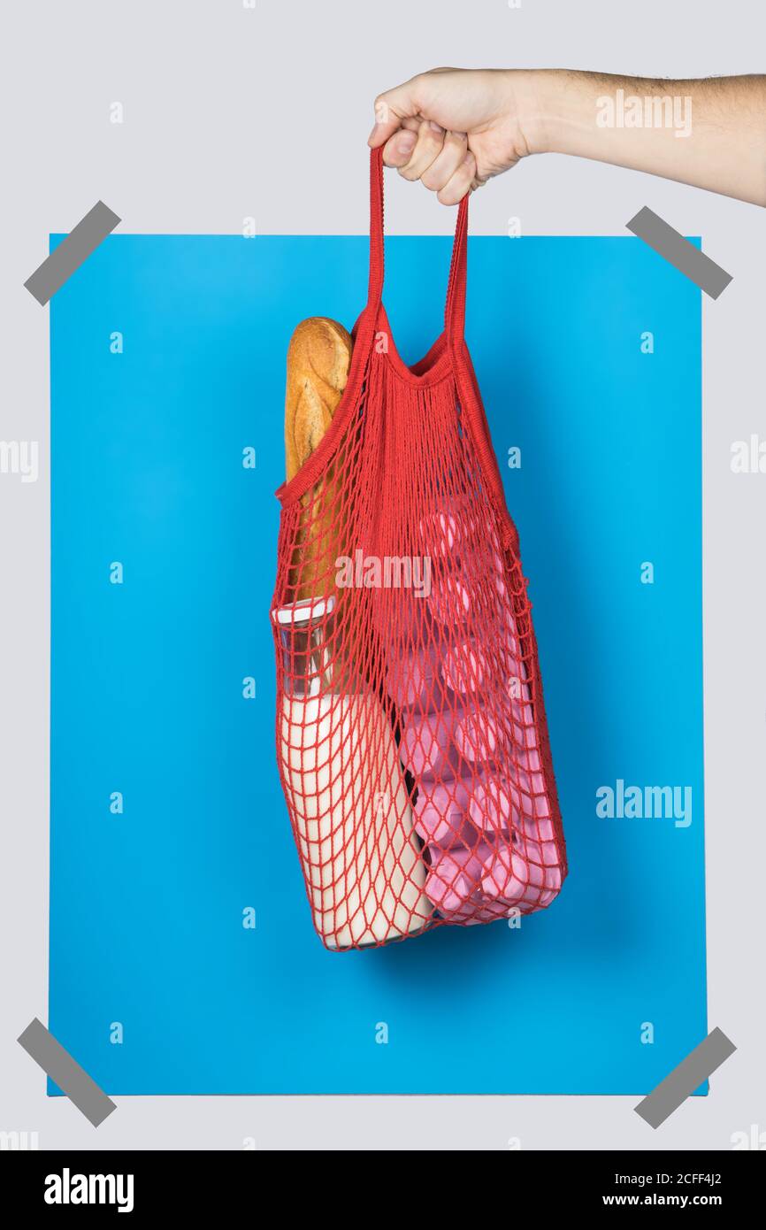 persona irriconoscibile che porta borsa a rete con vari generi alimentari contro il blu rettangolo durante lo shopping senza sprechi Foto Stock