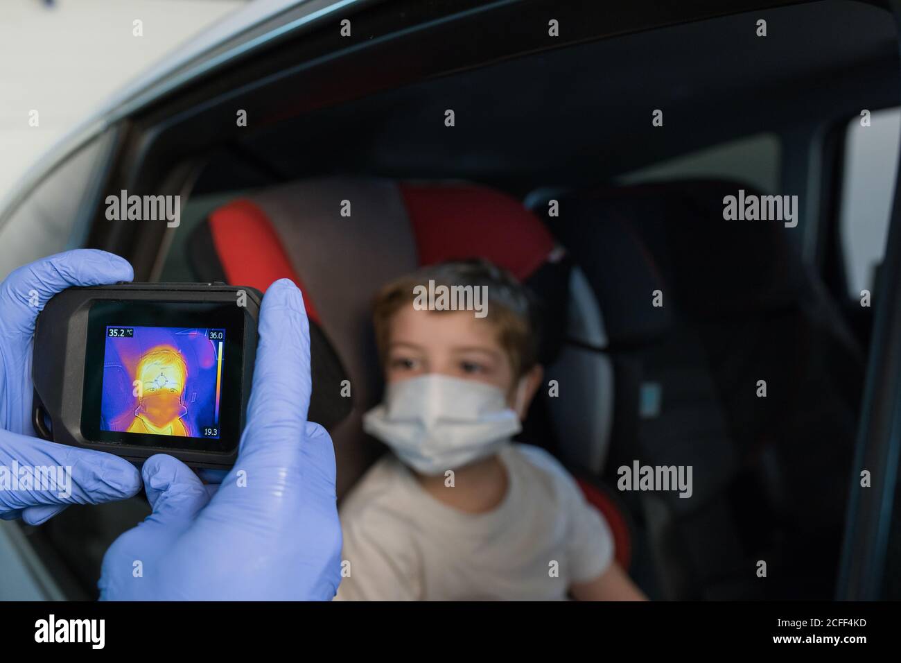 Crop medico in guanti medici misurazione della temperatura del ragazzo mentre utilizzo della telecamera a infrarossi durante l'epidemia di coronavirus Foto Stock