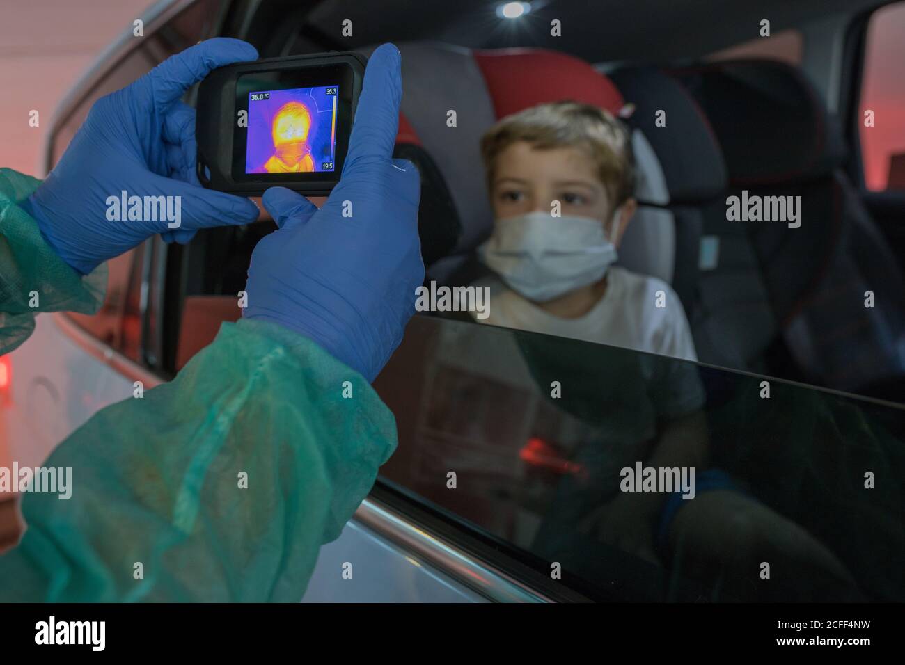 Crop medico in guanti medici misurazione della temperatura del ragazzo mentre utilizzo della telecamera a infrarossi durante l'epidemia di coronavirus Foto Stock