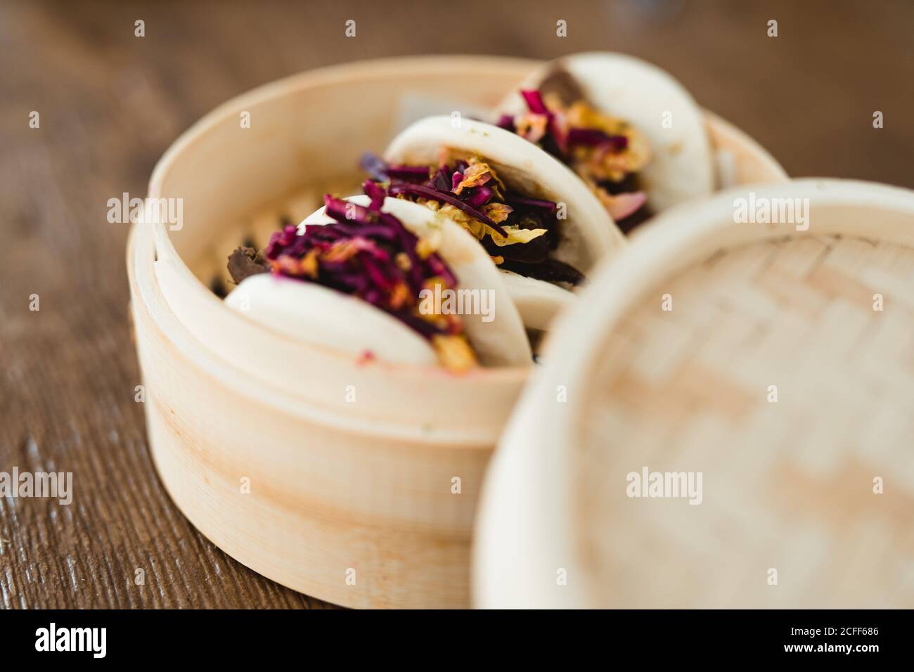 Primo piano di panino asiatico tradizionale cotto al vapore con carne e. verdure in vaporiera di bambù messo in tavola di legno Foto Stock