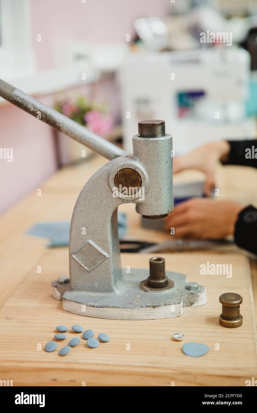 Crop persona anonima mani tirando la leva del costruttore di pulsanti su tavolo in laboratorio professionale di vestiario mentre si fa l'indumento Foto Stock