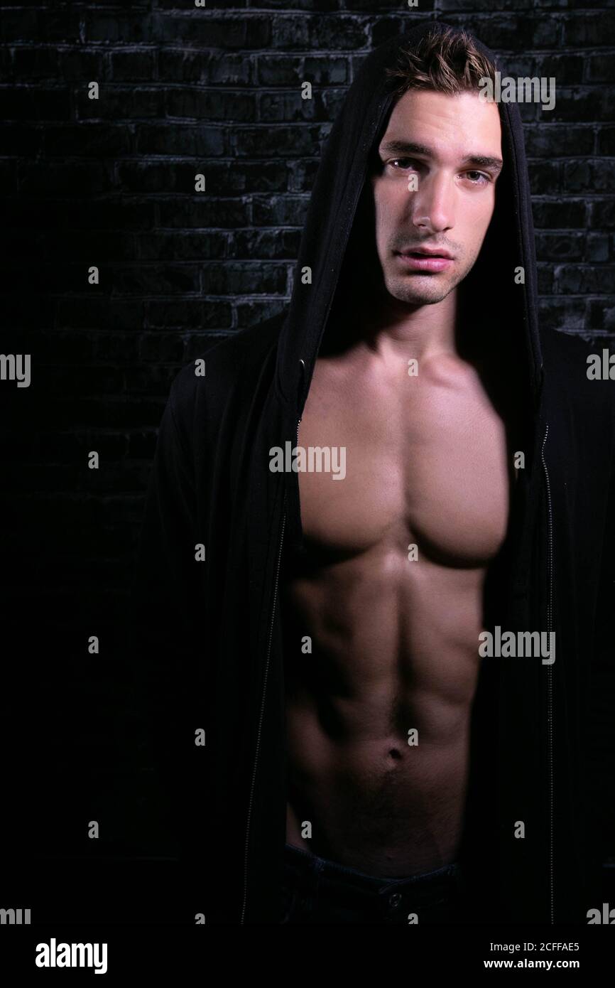 Ritratto di giovane attraente guardando la macchina fotografica con aperto felpa con cappuccio nera che rivela le specie muscolari e l'abs sixpack Foto Stock