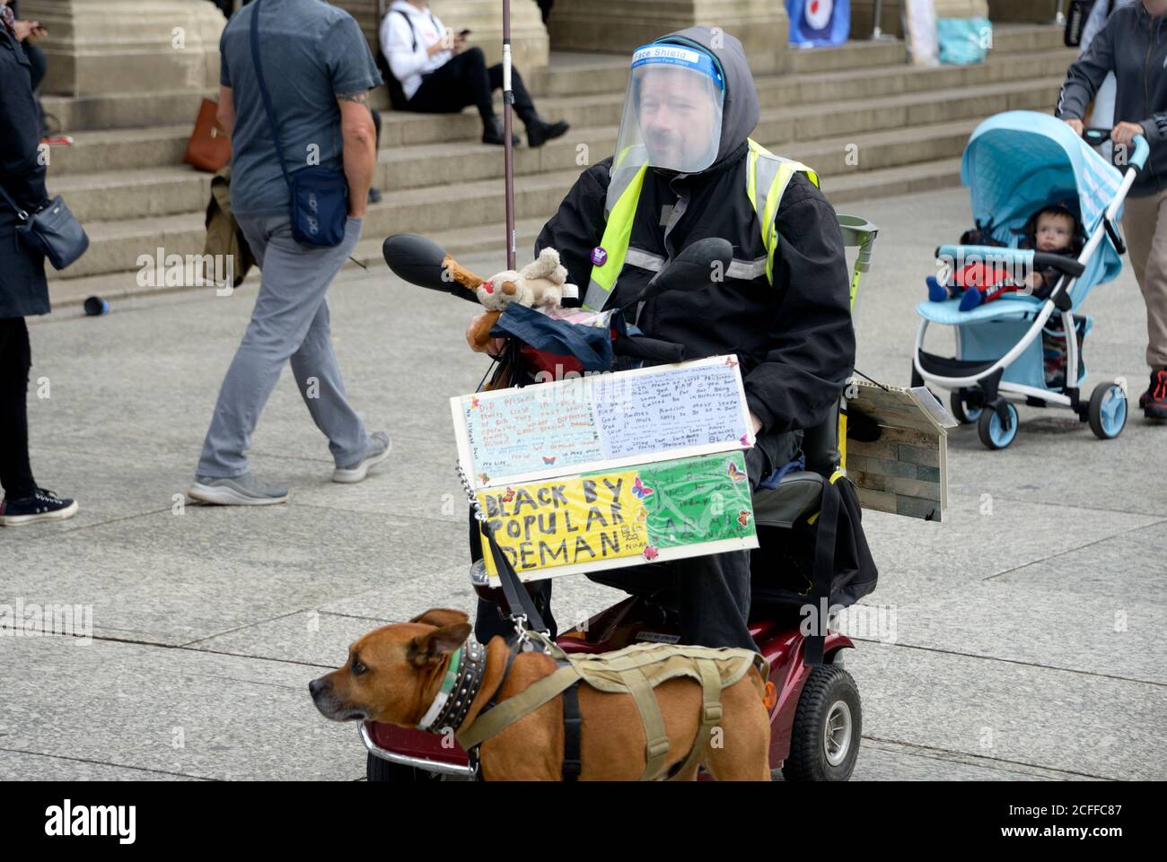 Uomo disabile, con visiera, su scooter mobile, con il suo cane. Foto Stock