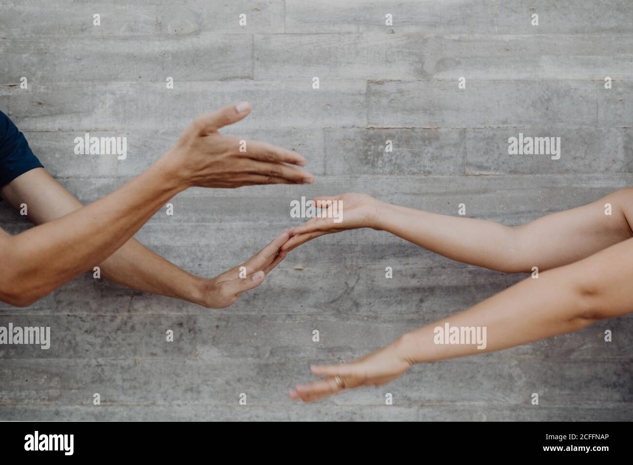 Mani forti abbronzate di uomo e donna di raccolto gesturing e mostrando su e giù su sfondo di parete grigia Foto Stock