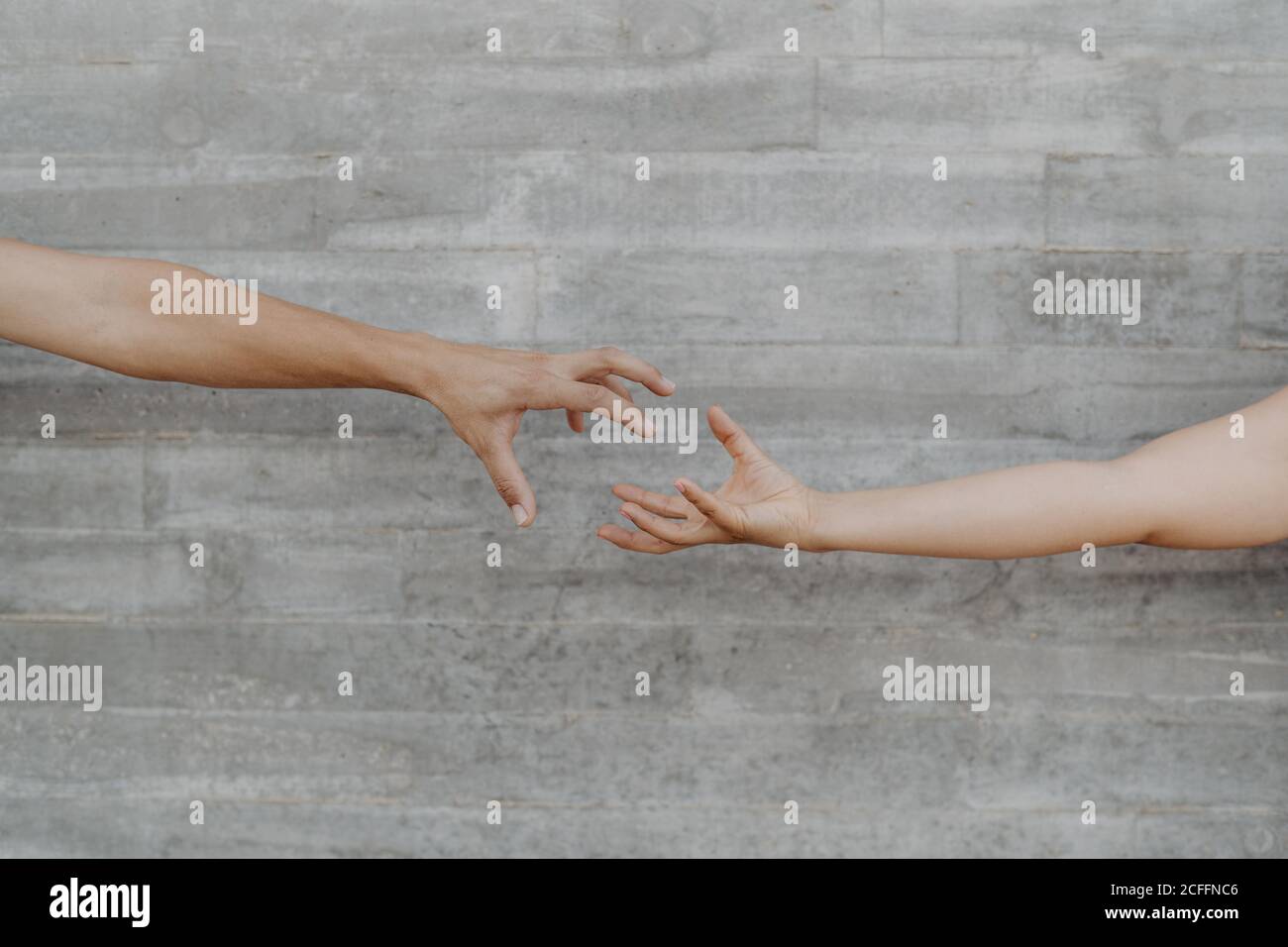 Mani forti abbronzate di uomo e donna di raccolto gesturing e mostrando l'azione di prendere su sfondo di parete grigia Foto Stock