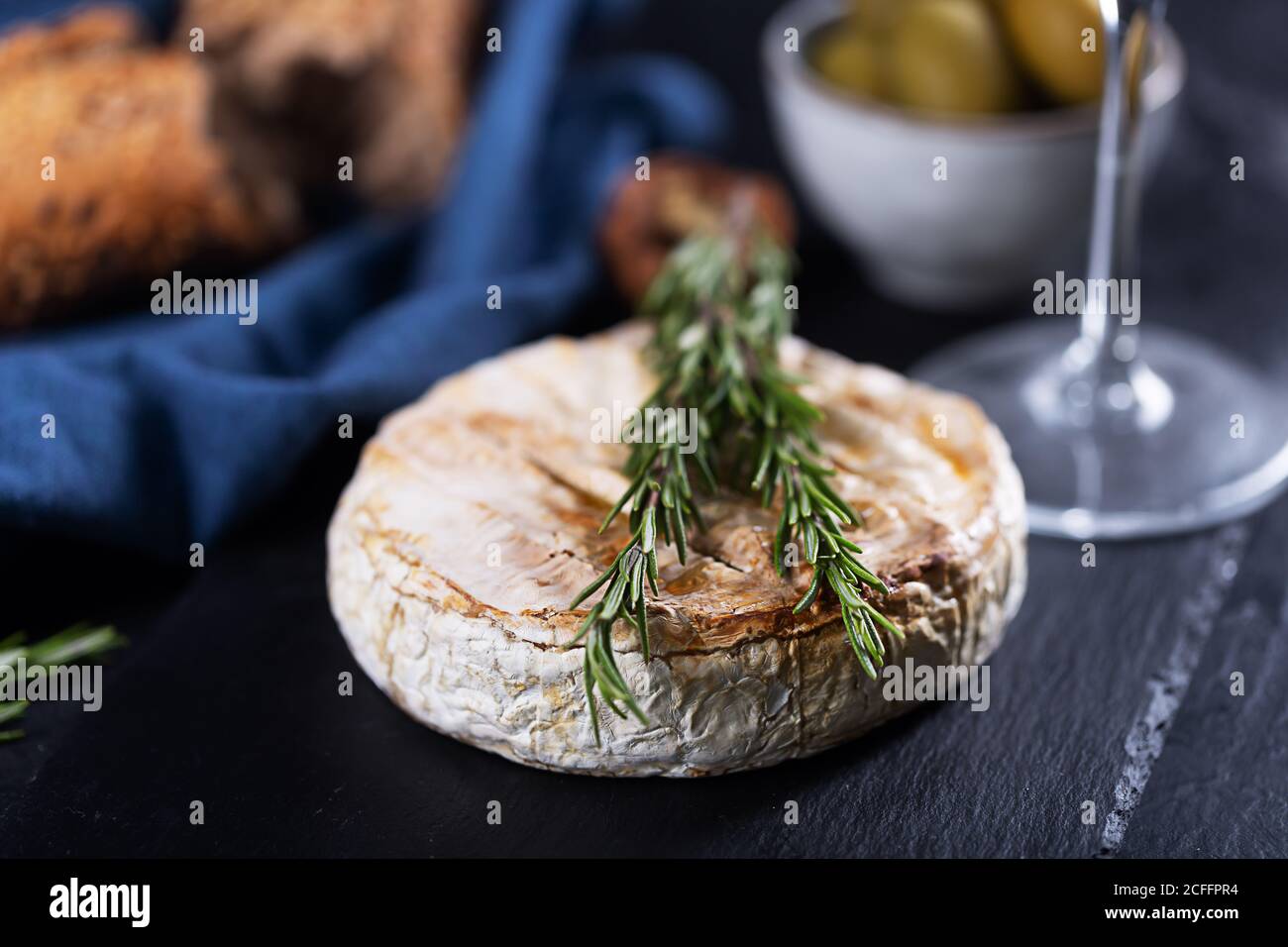 Formaggio camembert al forno con rosmarino, olive e pane su sfondo scuro, primo piano Foto Stock