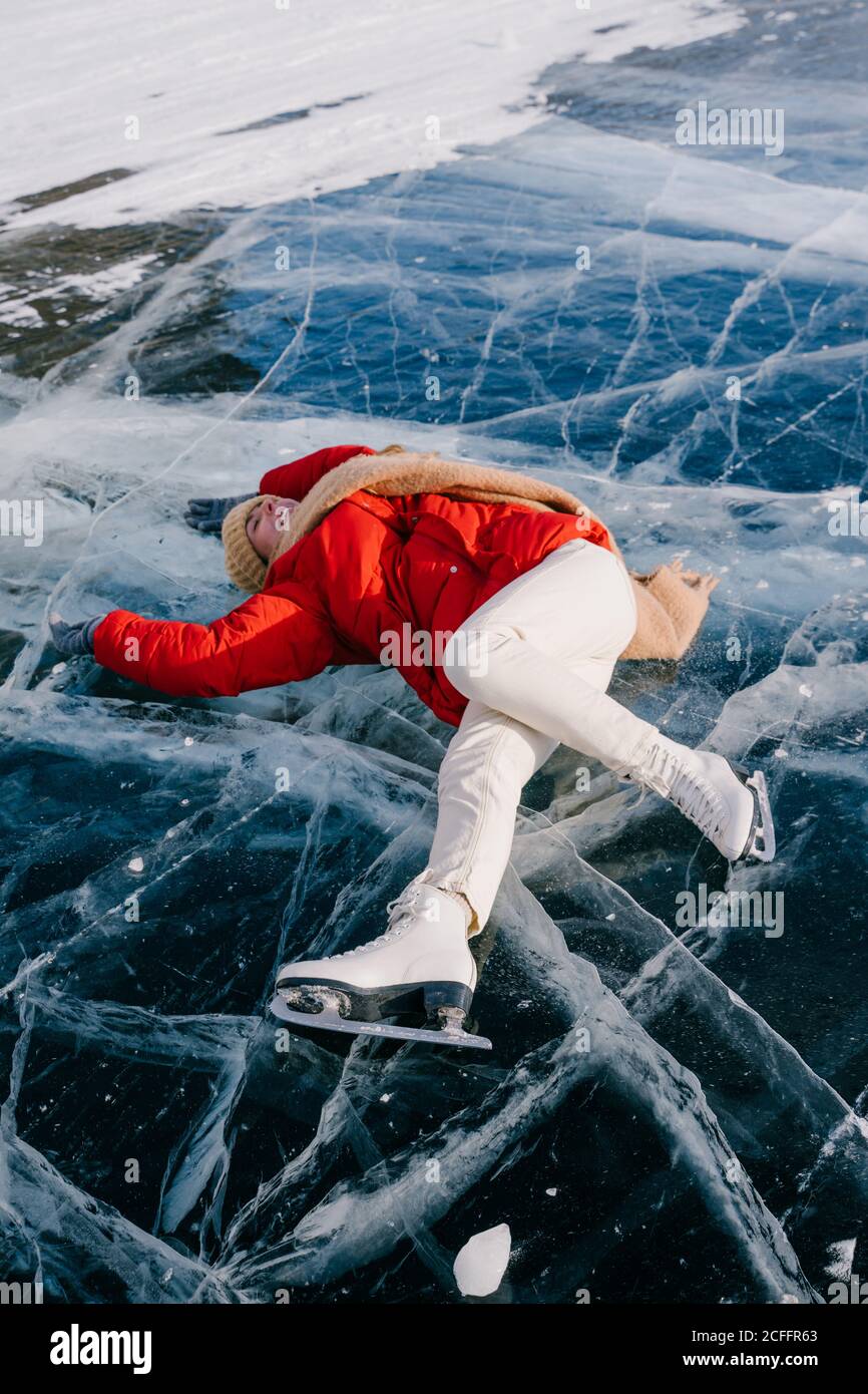 Dall'alto di felice giovane donna attiva in caldo attivo indossare e pattini sdraiati sul ghiaccio sul fiume congelato e. Godetevi una bella giornata invernale in Siberia Foto Stock