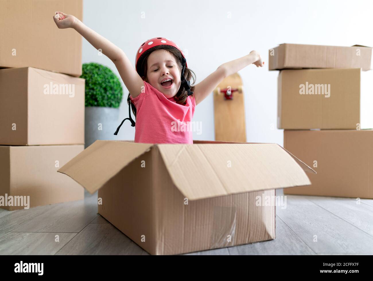 Felice bambina sorridendo e fissando il casco mentre si siede scatola di cartone e gioco durante il trasferimento Foto Stock