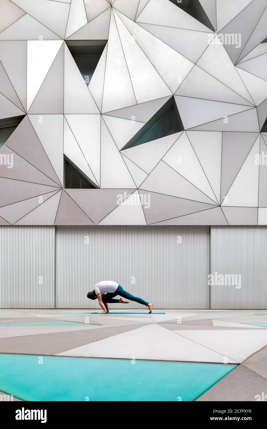 Vista laterale del maschio adulto in abbigliamento sportivo che fa la posizione della tavola allenamento da ginocchio a gomito mentre fai yoga contro la parete geometrica camera spaziosa Foto Stock
