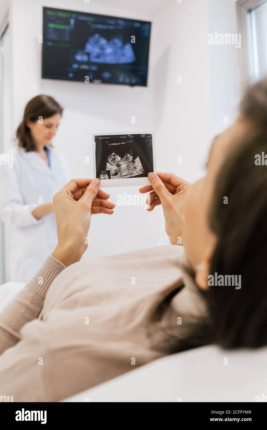 donna incinta non riconoscibile che ispeziona l'immagine dell'ecogramma mentre si sdraia sul letto nel reparto della clinica moderna di fertilità Foto Stock