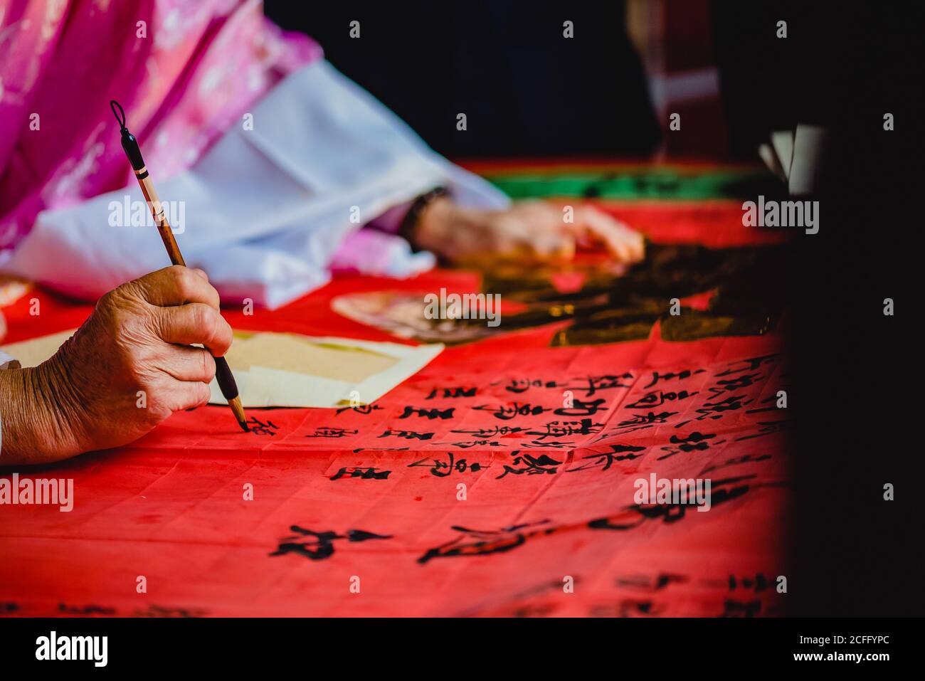 Crop master in kimono pittura nero geroglifi con inchiostro su Tessuto rosso nel tempio di Hong Kong Foto Stock