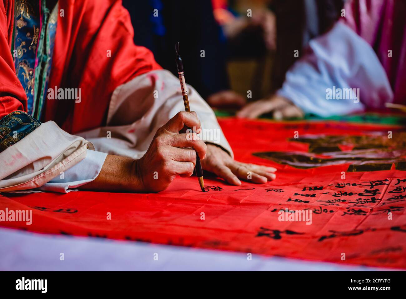 Crop master in kimono pittura nero geroglifi con inchiostro su Tessuto rosso nel tempio di Hong Kong Foto Stock