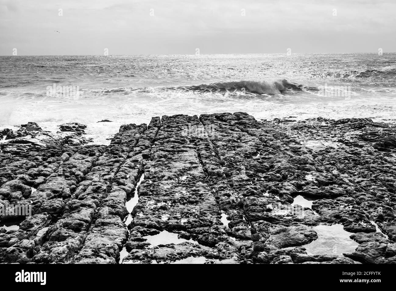 Pietre bianche e nere sulla tranquilla riva dell'oceano con le onde in esecuzione in giornata di sole Foto Stock