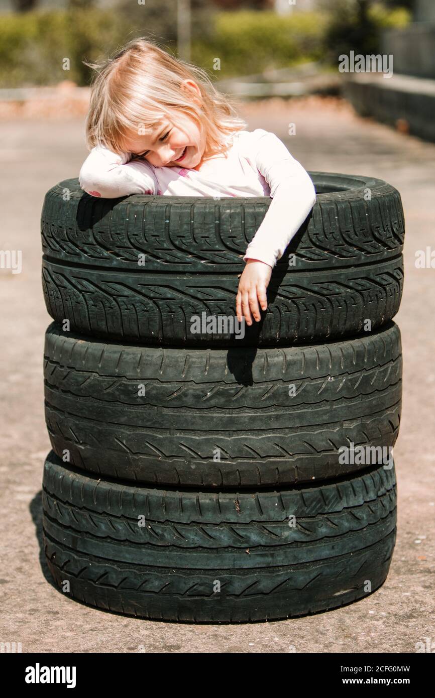 Felice adorabile bambina che riposa in pila di pneumatici per auto durante il giorno d'estate potrai divertirti e giocare all'aperto Foto Stock