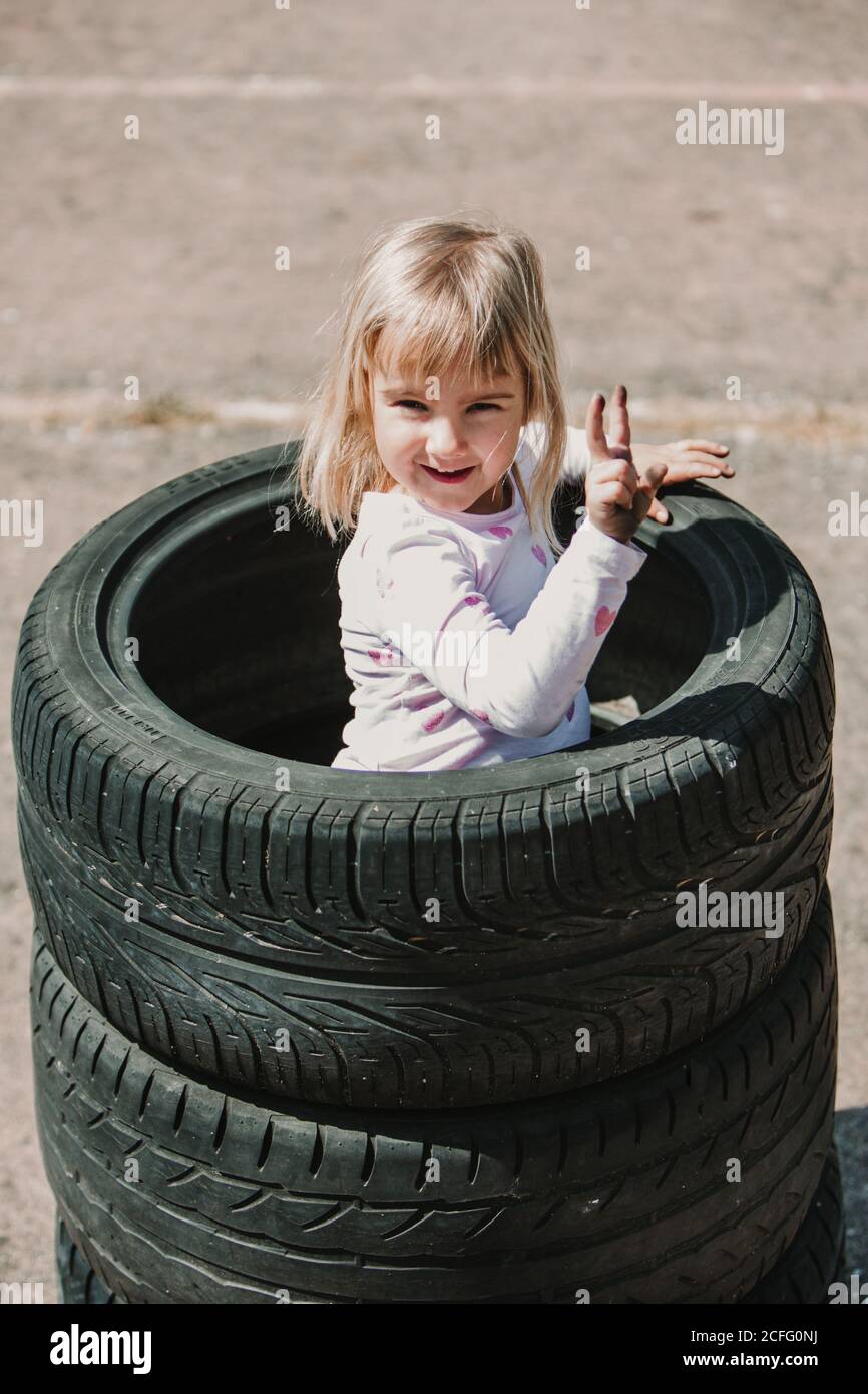 Dall'alto di felice adorabile bambina in piedi in pila di pneumatici per auto mentre si divertono e si gioca all'aperto giorno d'estate Foto Stock