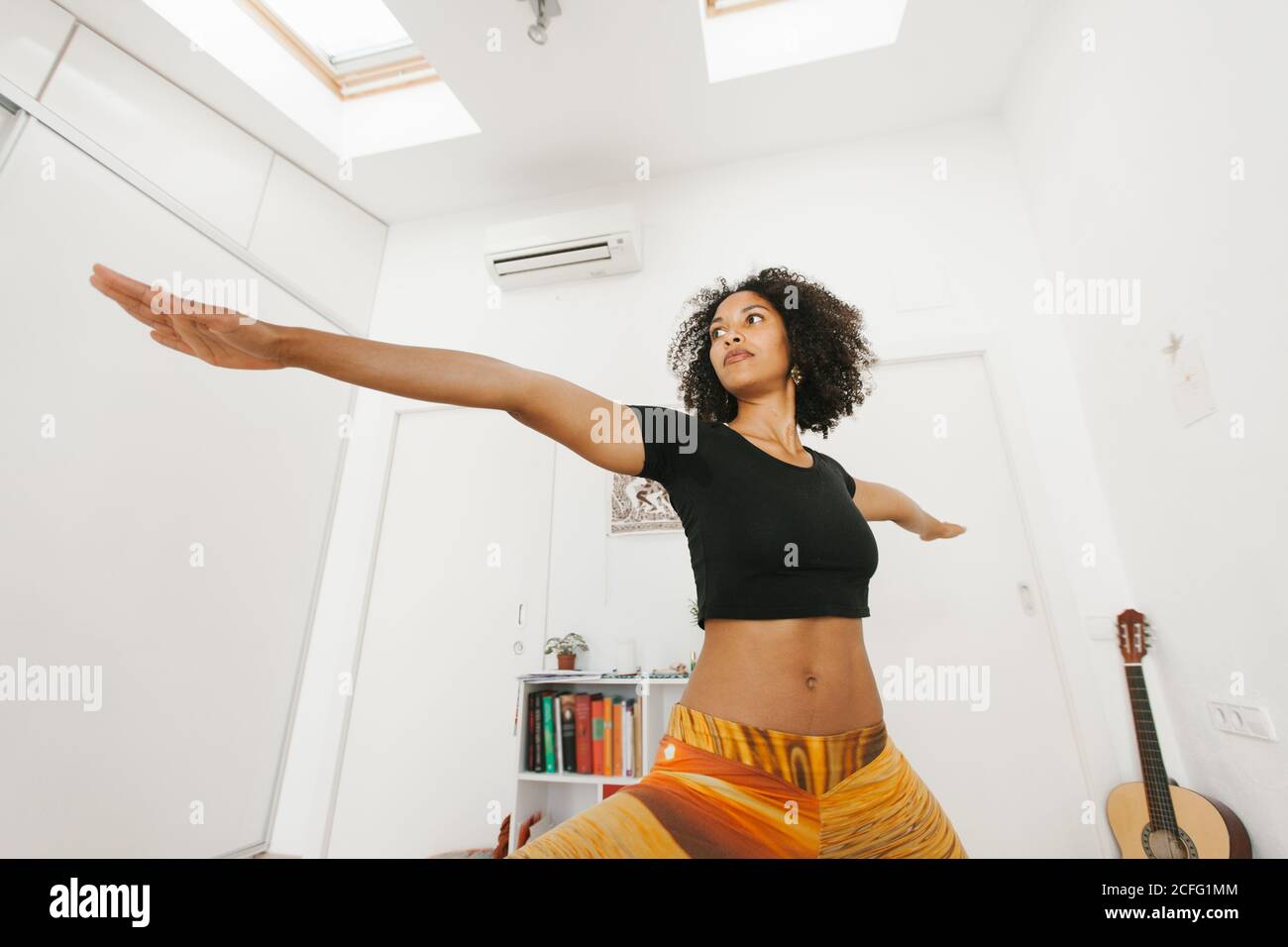 African American attraente giovane donna che esegue la postura di yoga con le braccia allungate sul tappetino in stanza leggera Foto Stock