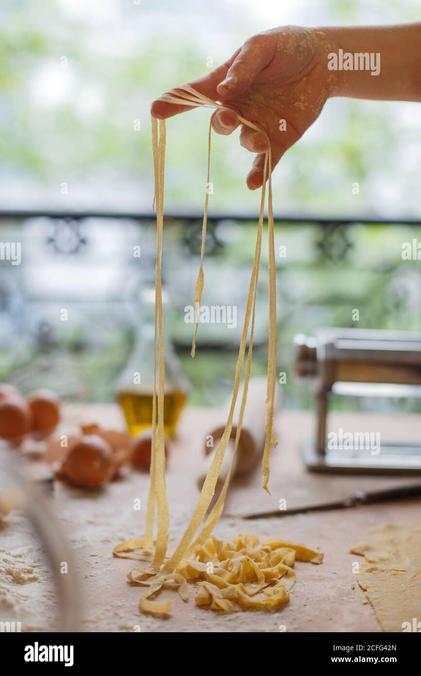 Donna che sta tagliando sottili strisce di pasta in mani mentre preparazione del pasto in cucina Foto Stock