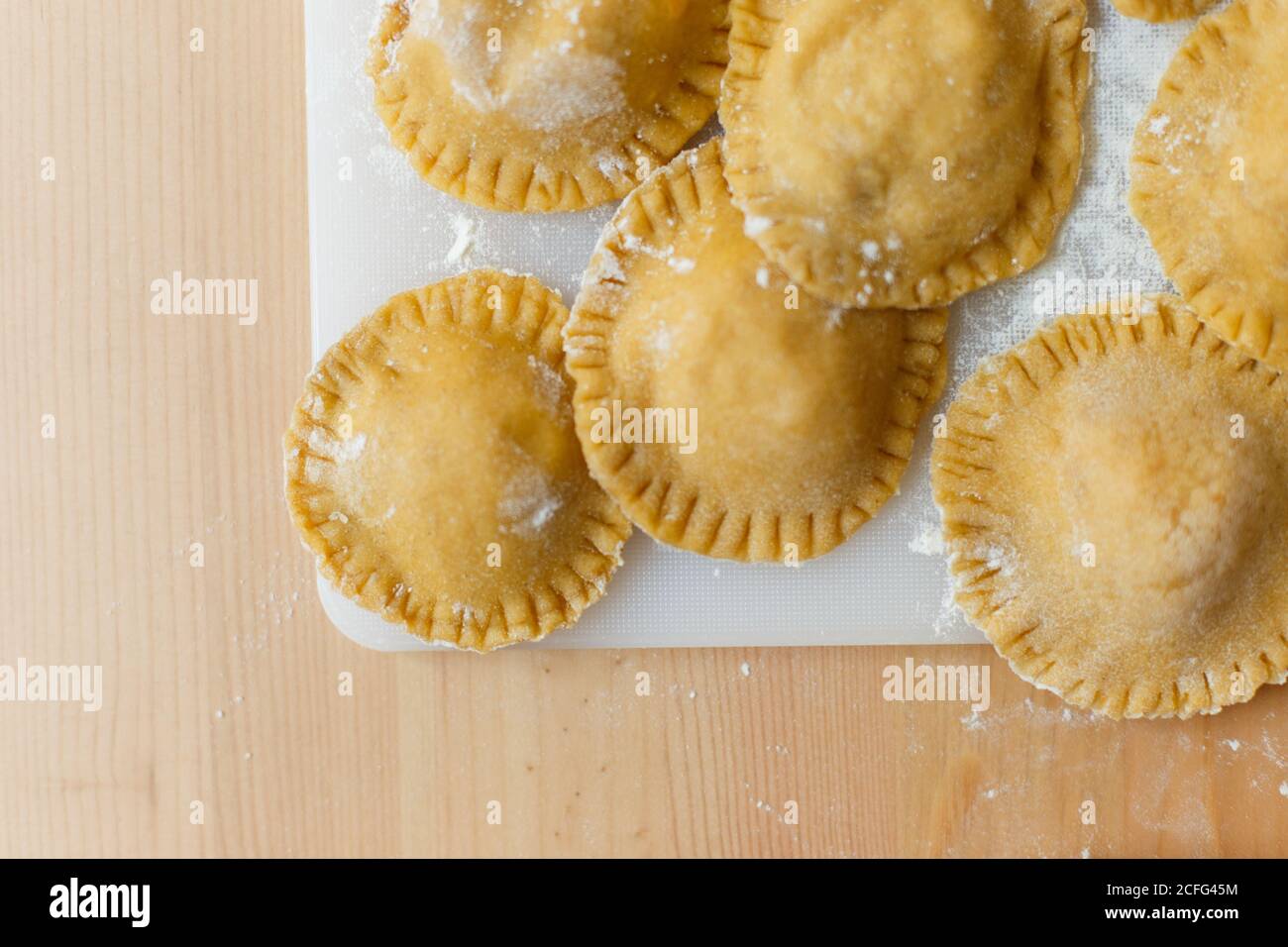 Dall'alto del tagliere con ravioli grezzi e rotondi su tavola di legno sullo sfondo di una bottiglia di oliva sfocata olio e ciotola con zucca ripieno in cucina Foto Stock