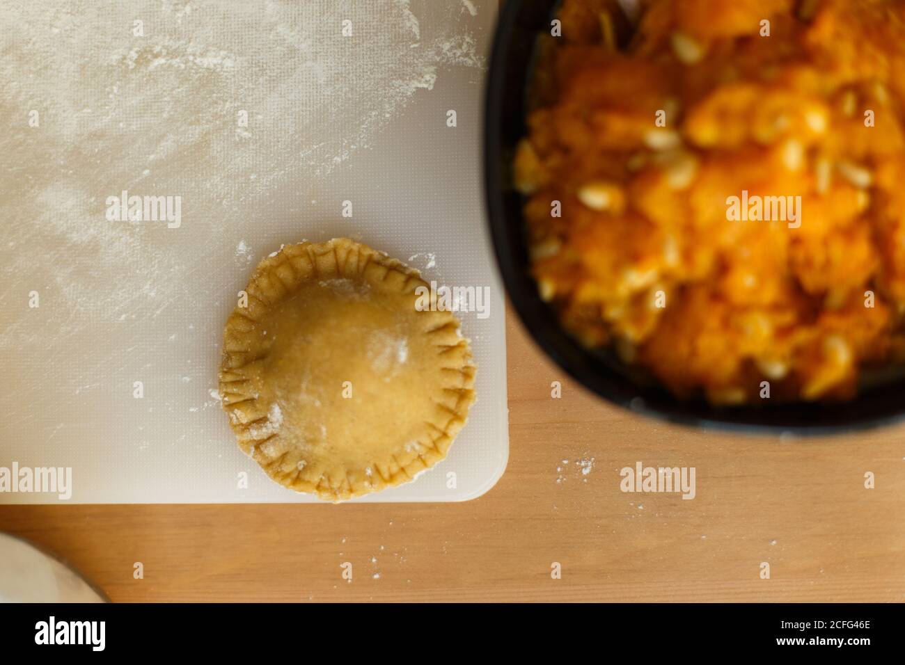 Vista dall'alto della ciotola con delizioso ripieno di ravioli purea di zucca e noci sul tavolo vicino al pezzo di impasto vaso di farina e tagliere con olio d'oliva crudo ravioli Foto Stock