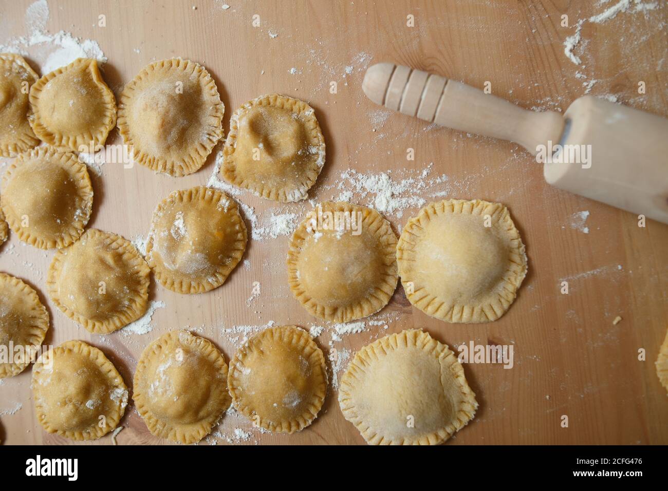 Dall'alto del tagliere con ravioli grezzi e rotondi su tavola di legno sullo sfondo di una bottiglia di oliva sfocata olio e ciotola con zucca ripieno in cucina Foto Stock